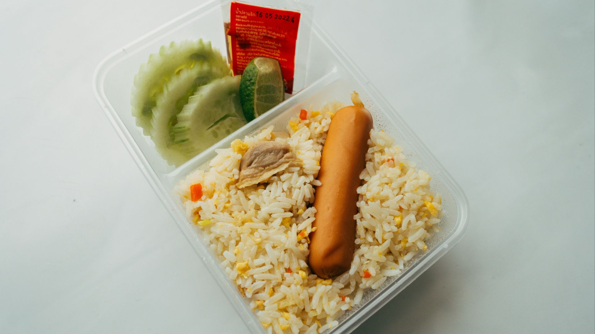 a plastic container filled with rice and a hot dog