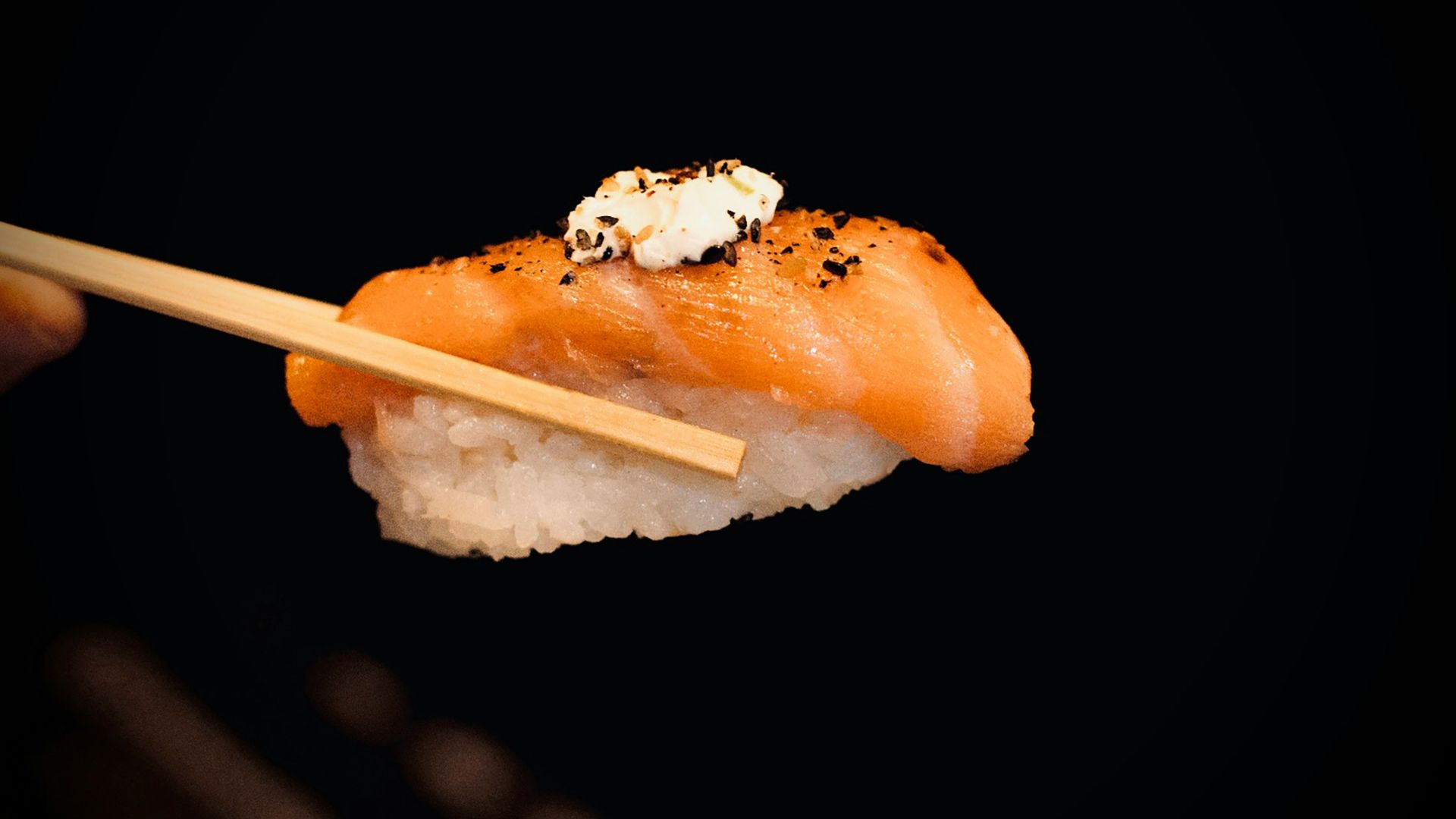 a person holding a piece of sushi with chopsticks