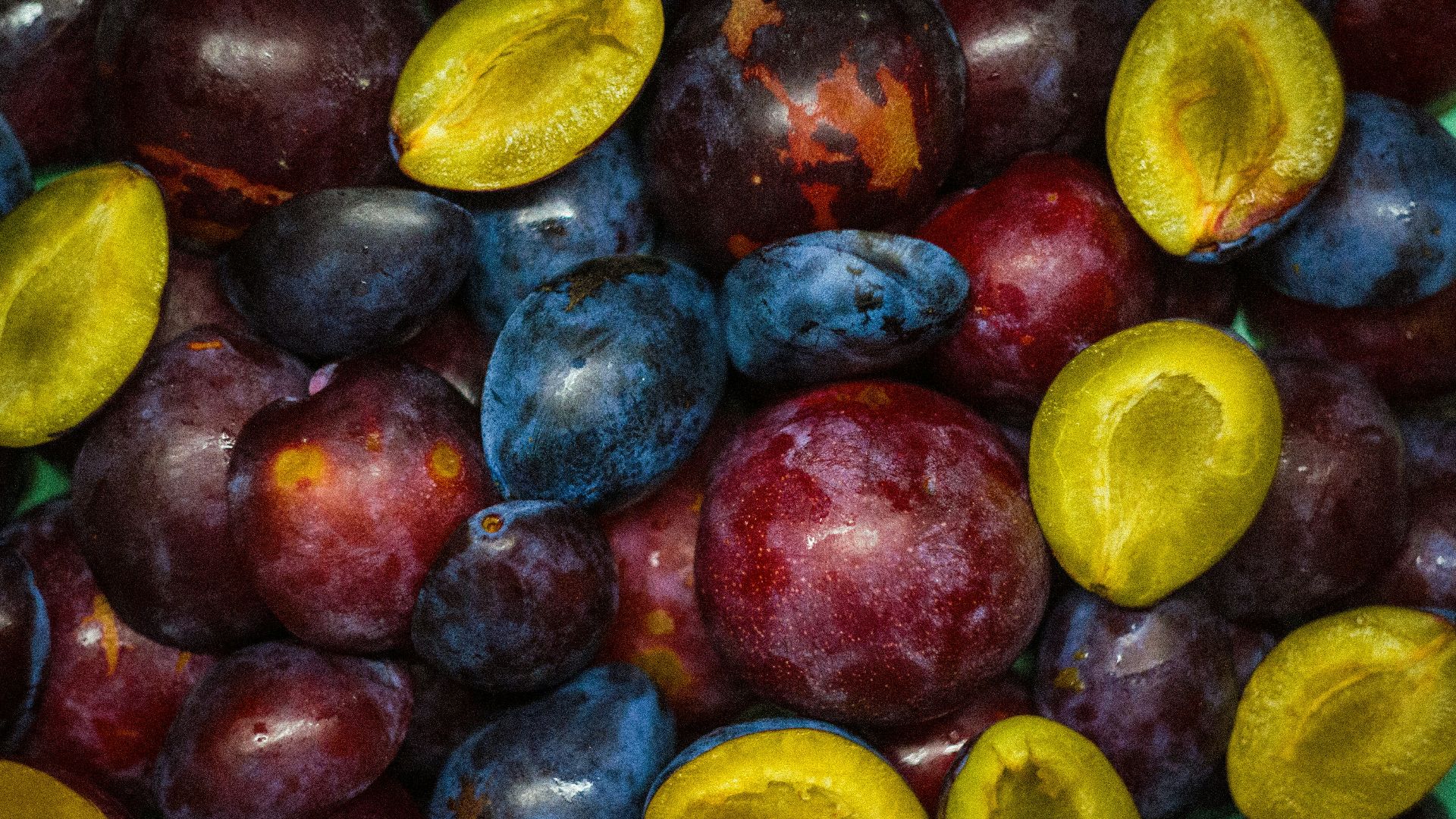 a pile of plums and plums with one cut in half