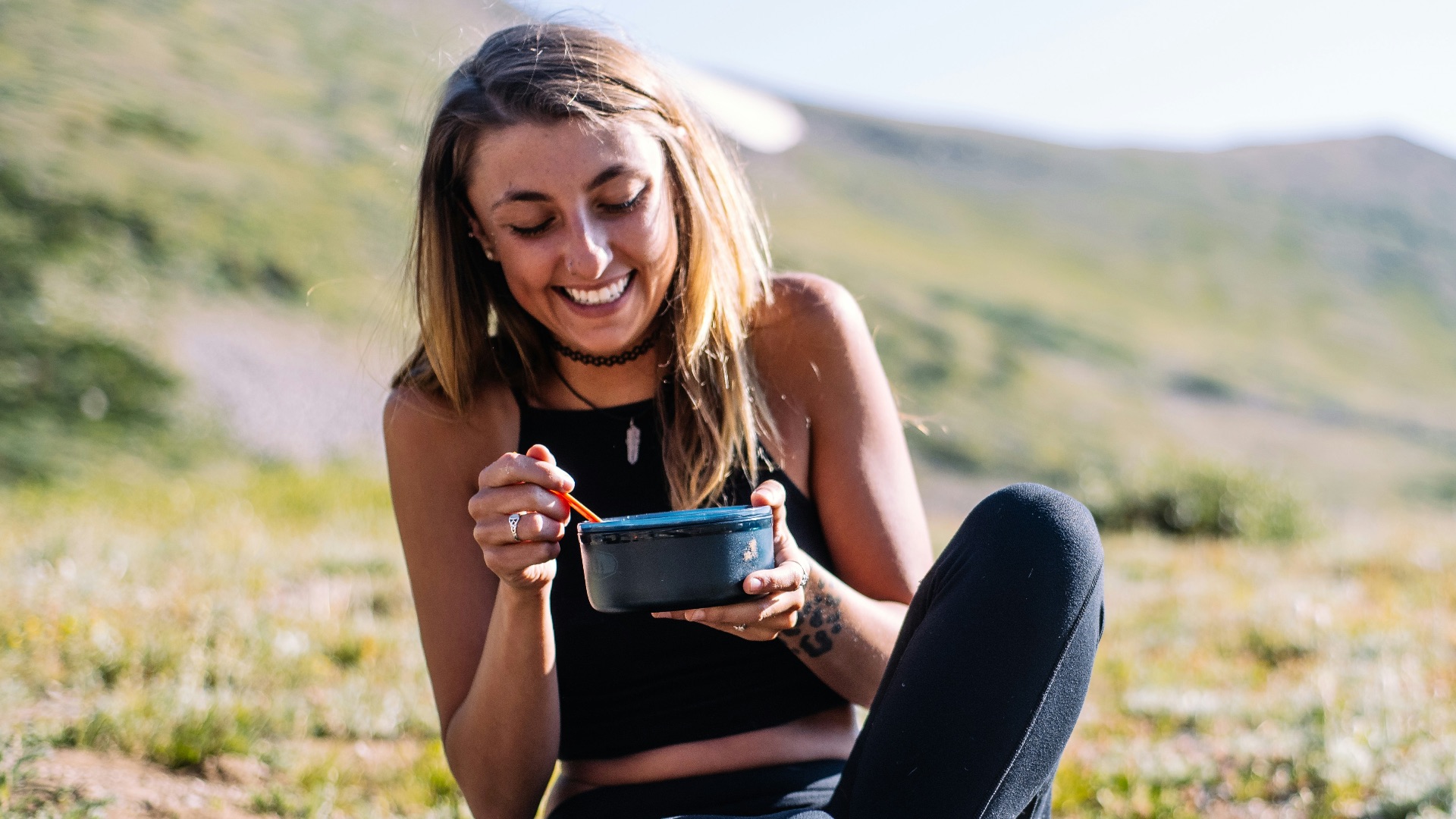woman in black tank top and black pants sitting on ground holding blue ceramic mug during