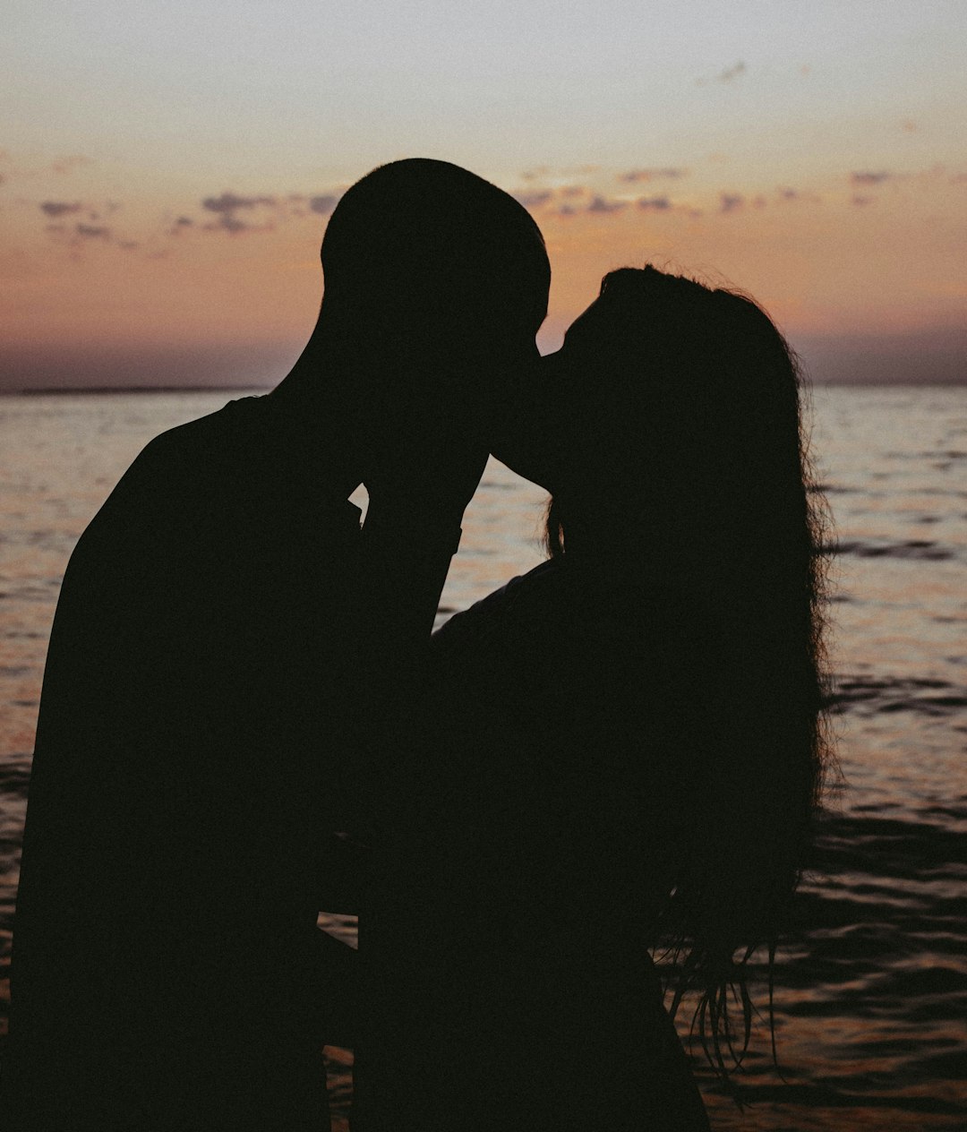 a man and a woman kissing in front of a body of water