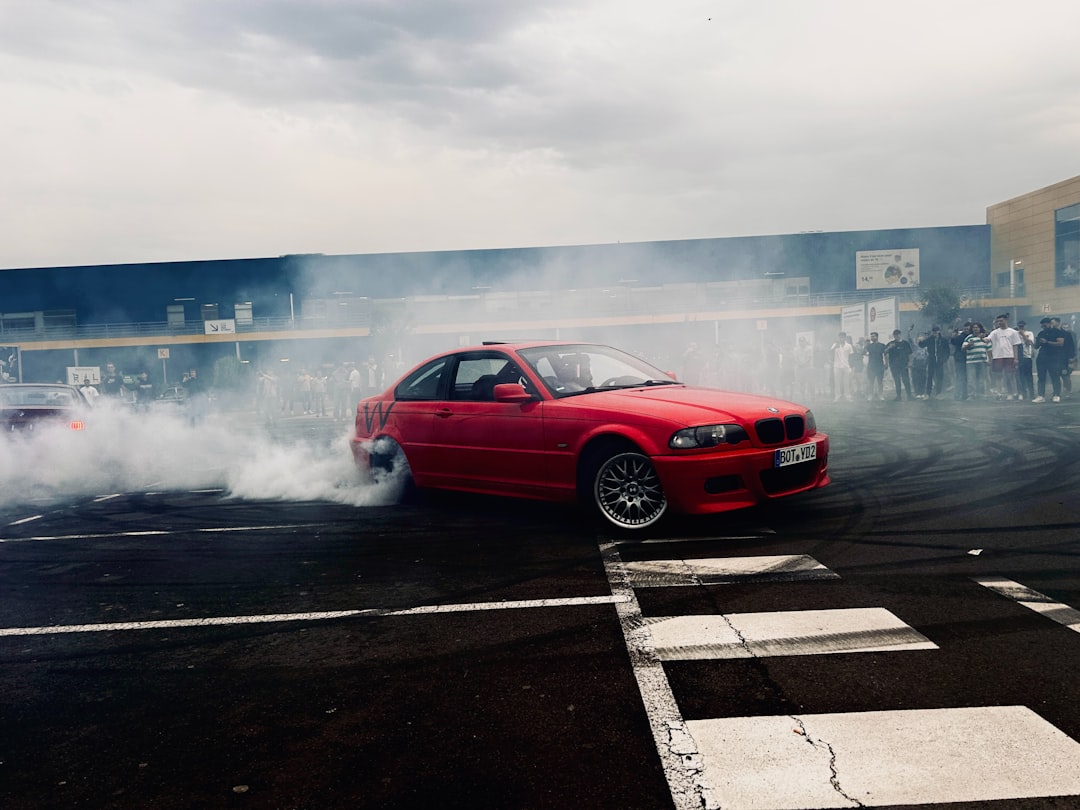 A red car driving down a street next to a crowd of people