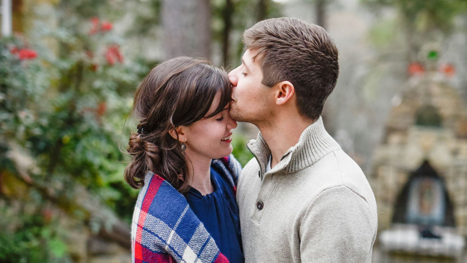 man kissing on woman forehead standing near tree during daytime