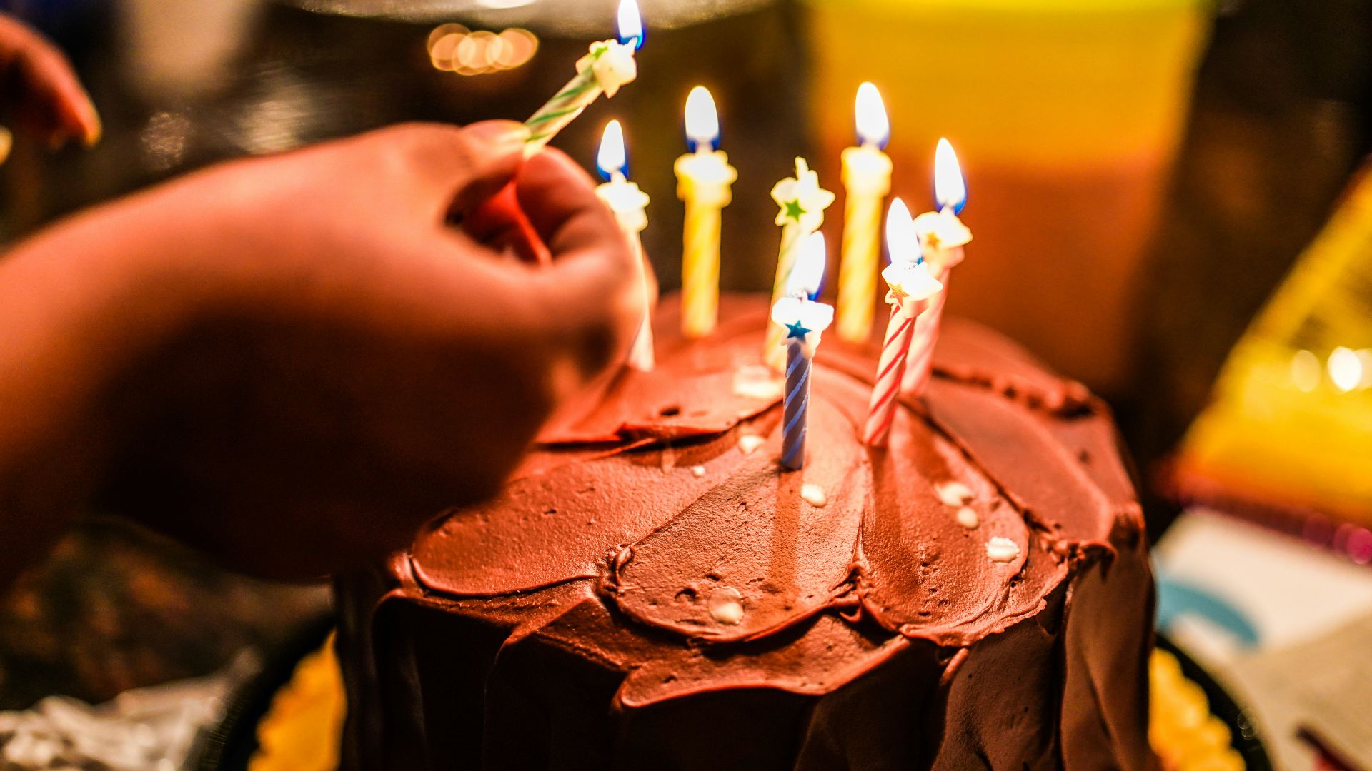 person holding lighted candle on brown cake