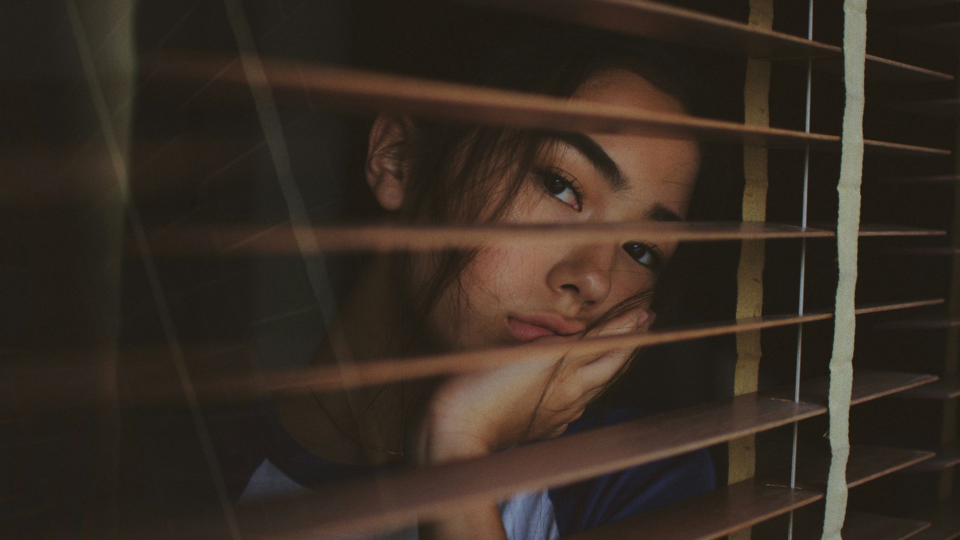 a woman looking out of a window with blinds