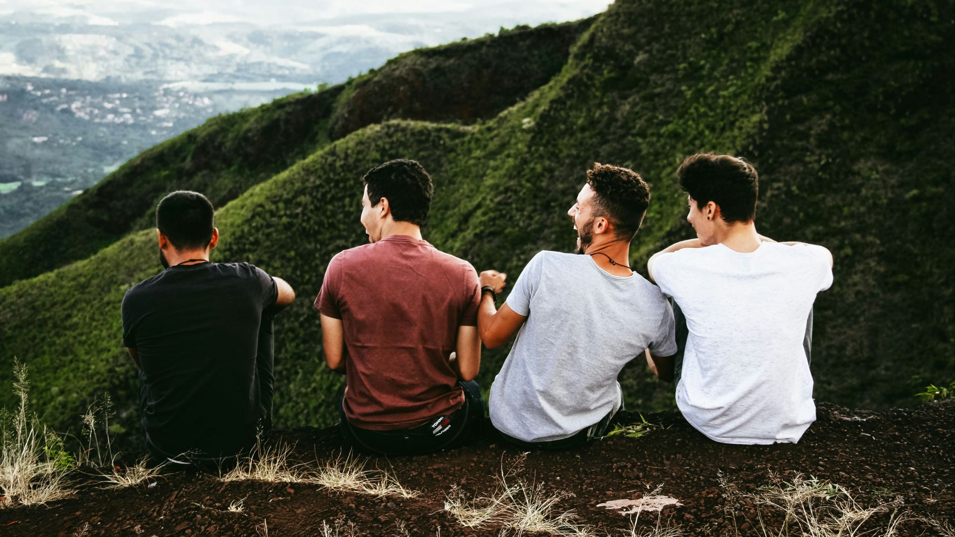 row of four men sitting on mountain trail
