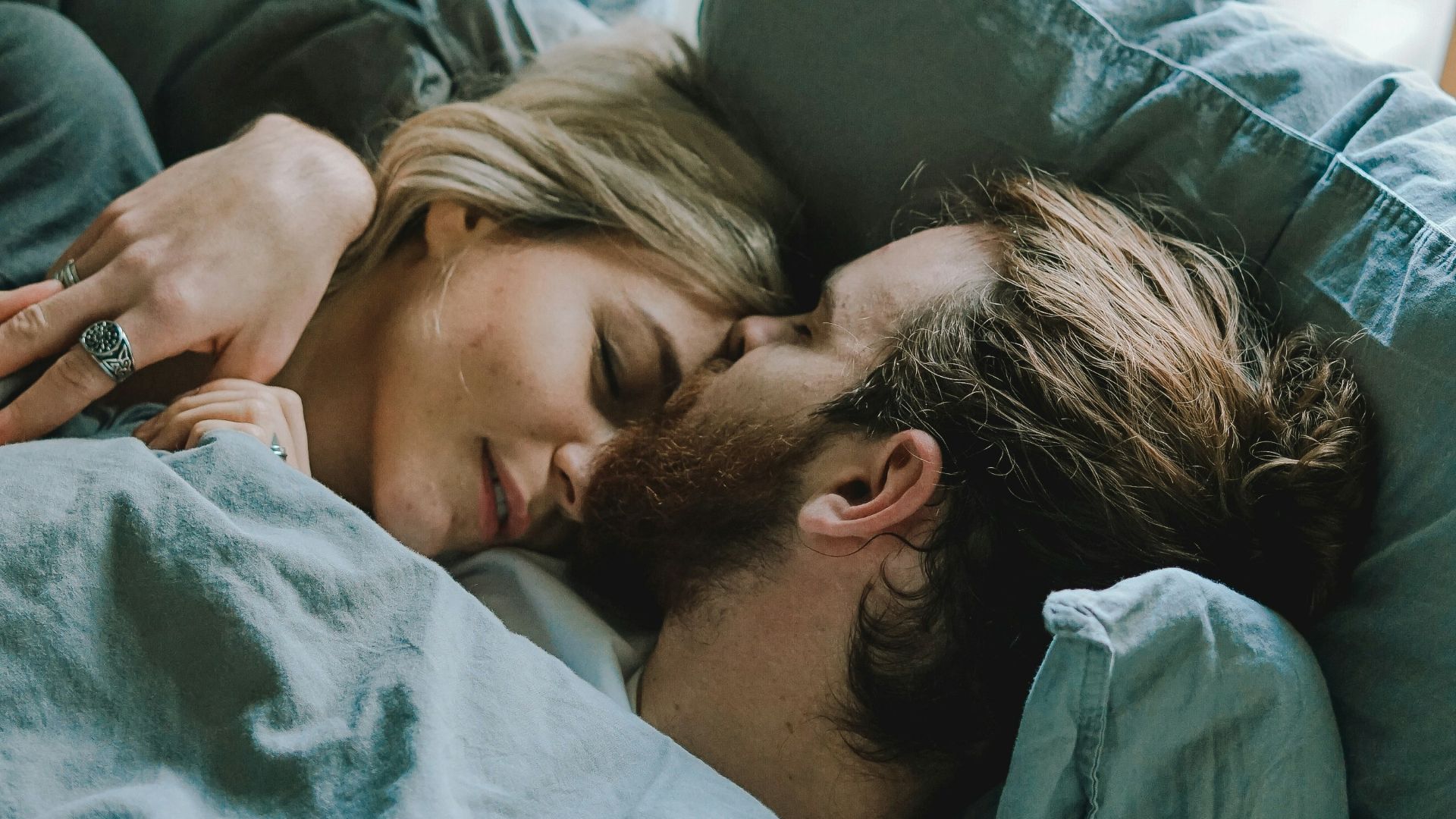 man kissing woman's forehead while lying on bed