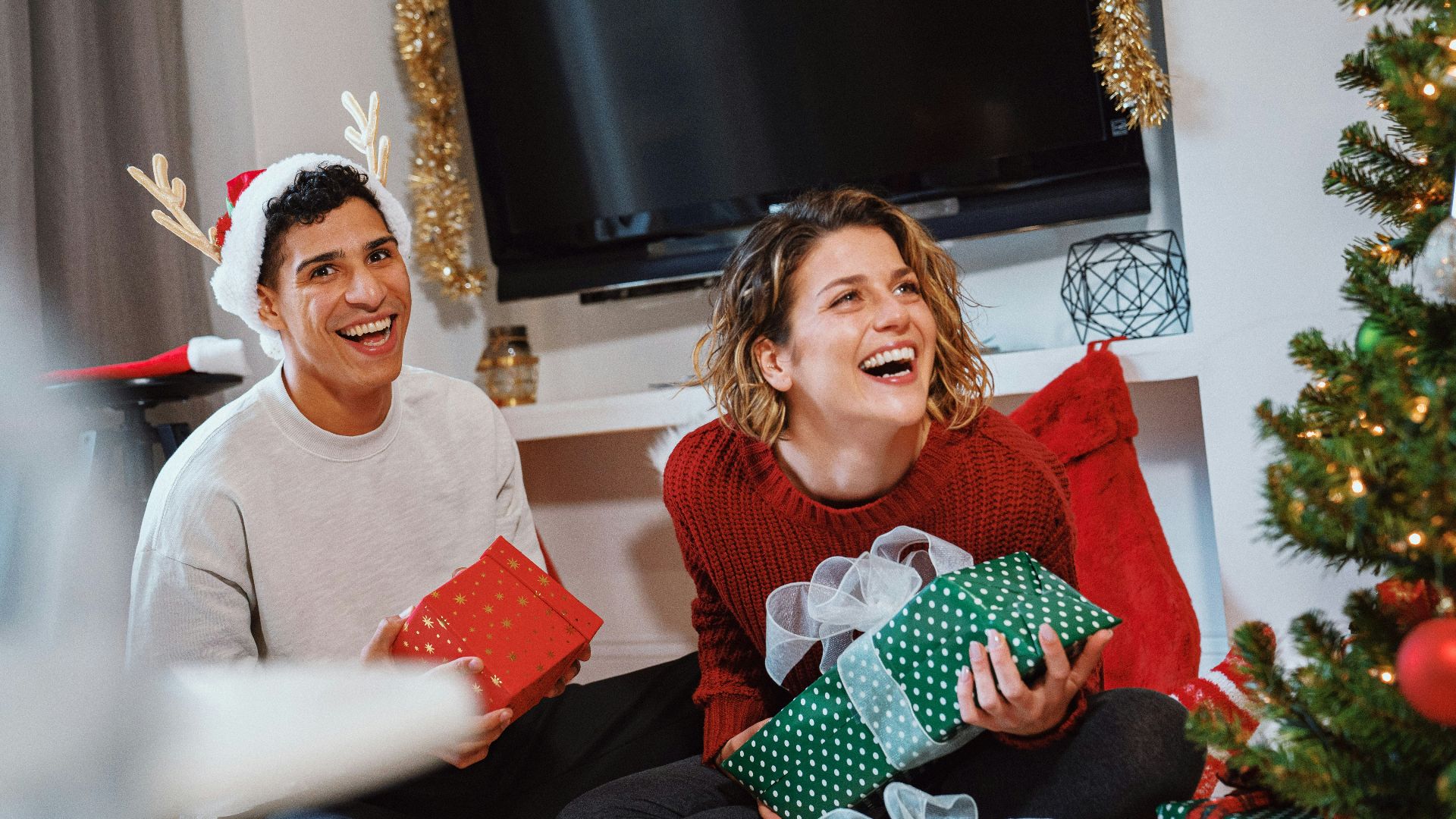 a person and a girl sitting on a couch with presents in front of a christmas tree