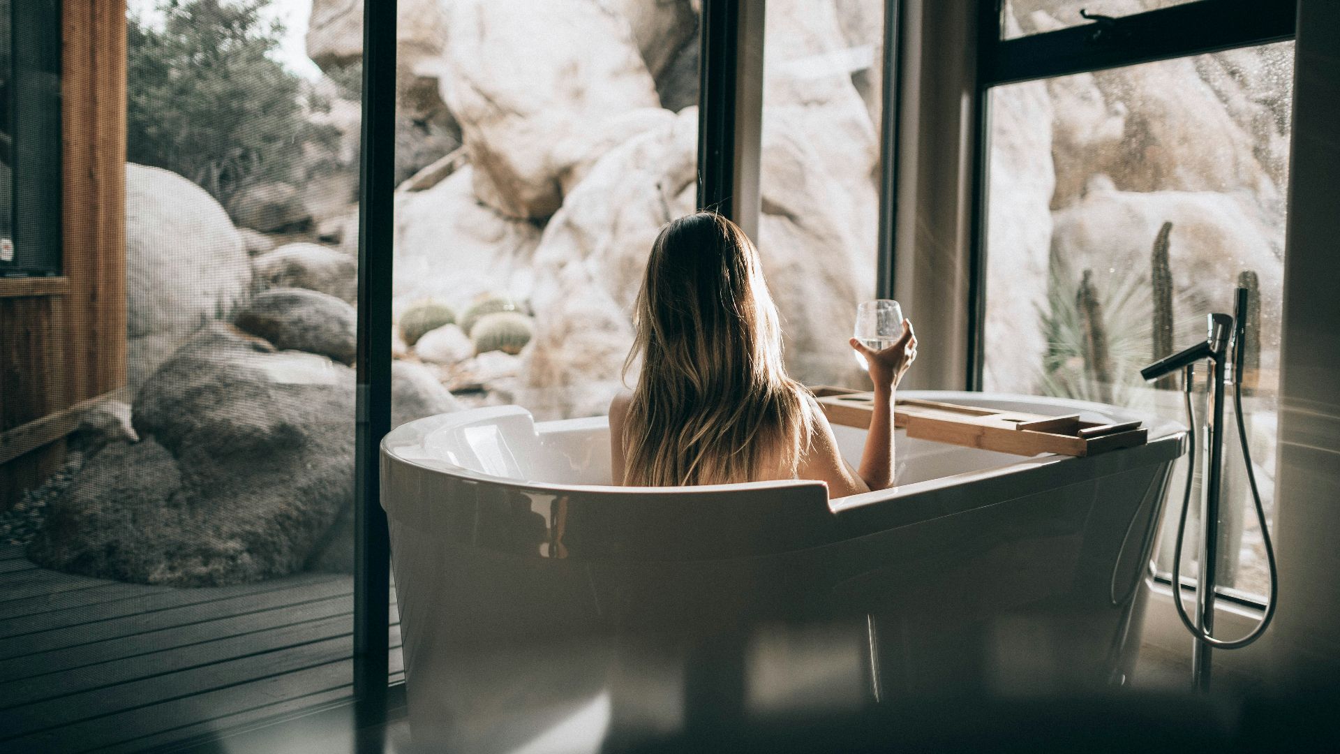 woman in white bathtub holding clear drinking glass