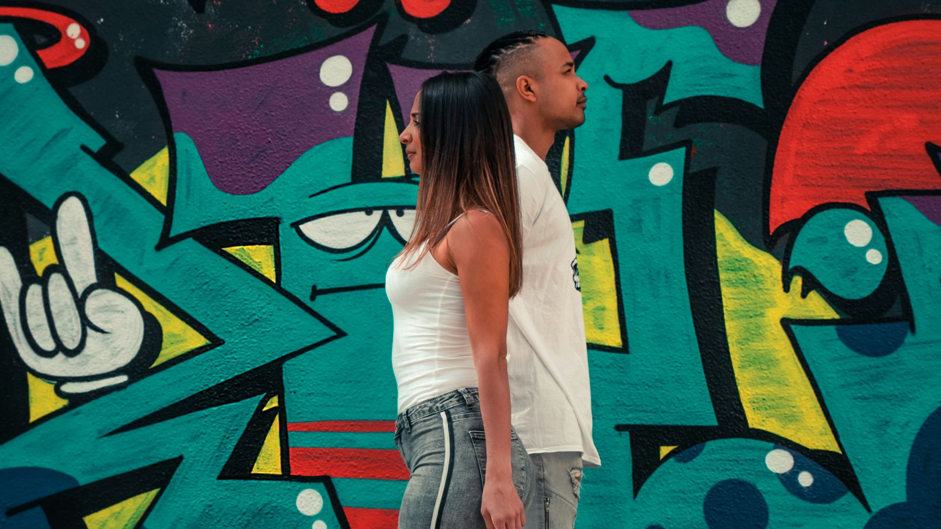 woman in white tank top and gray denim jeans standing beside graffiti wall