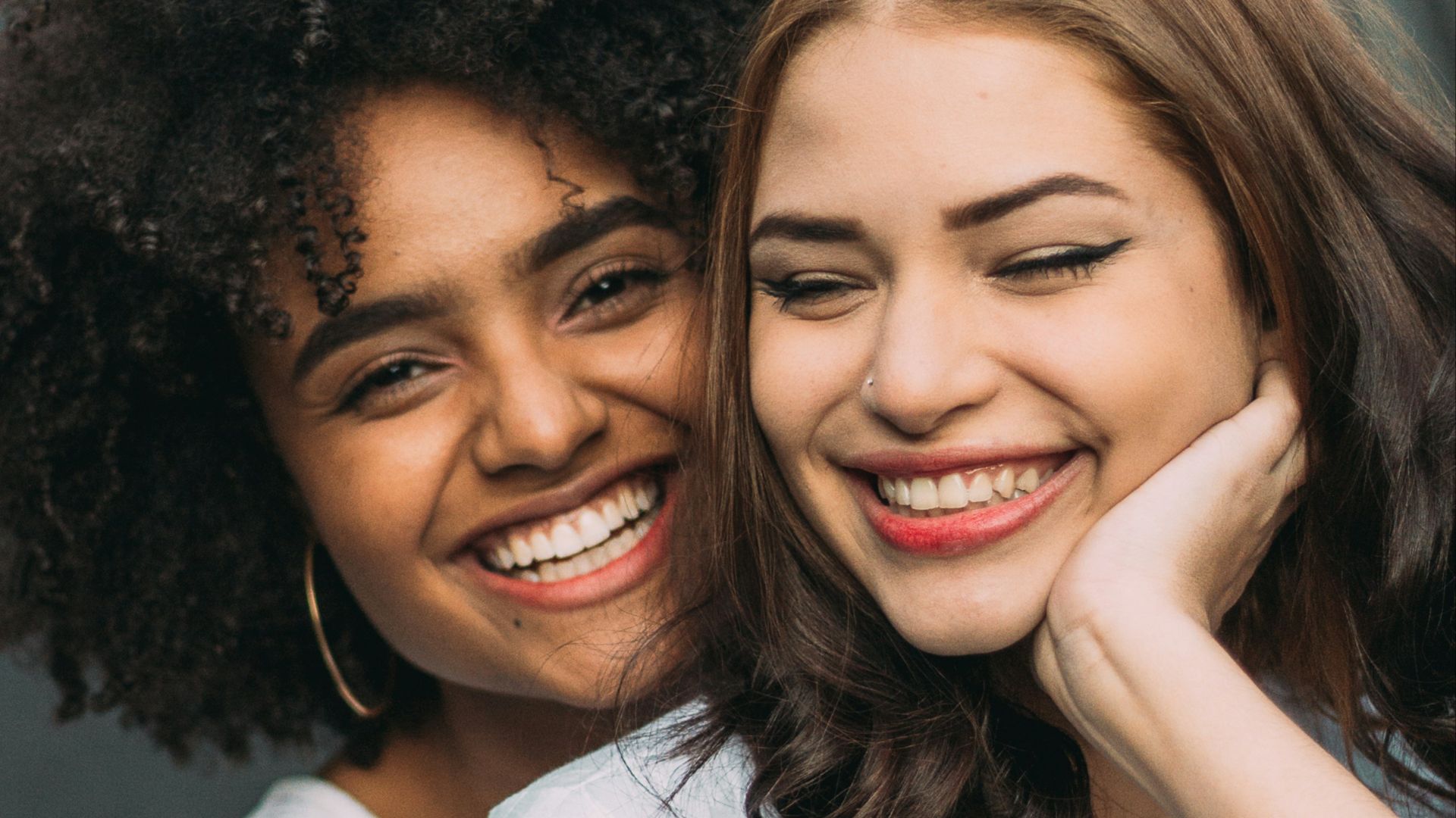 two smiling woman standing near white wall