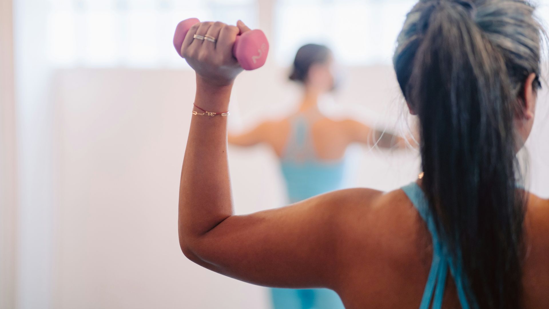 woman in blue tank top holding pink dumbbell