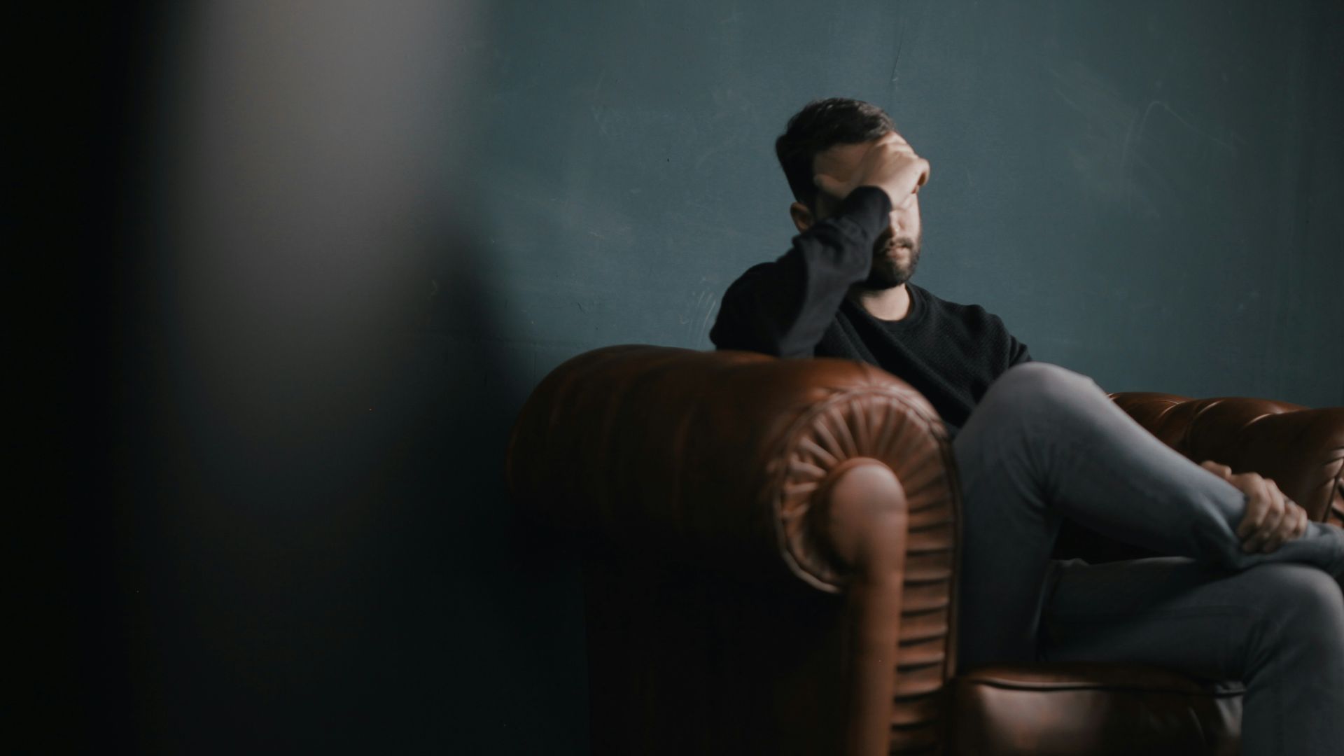 a man holds his head while sitting on a sofa