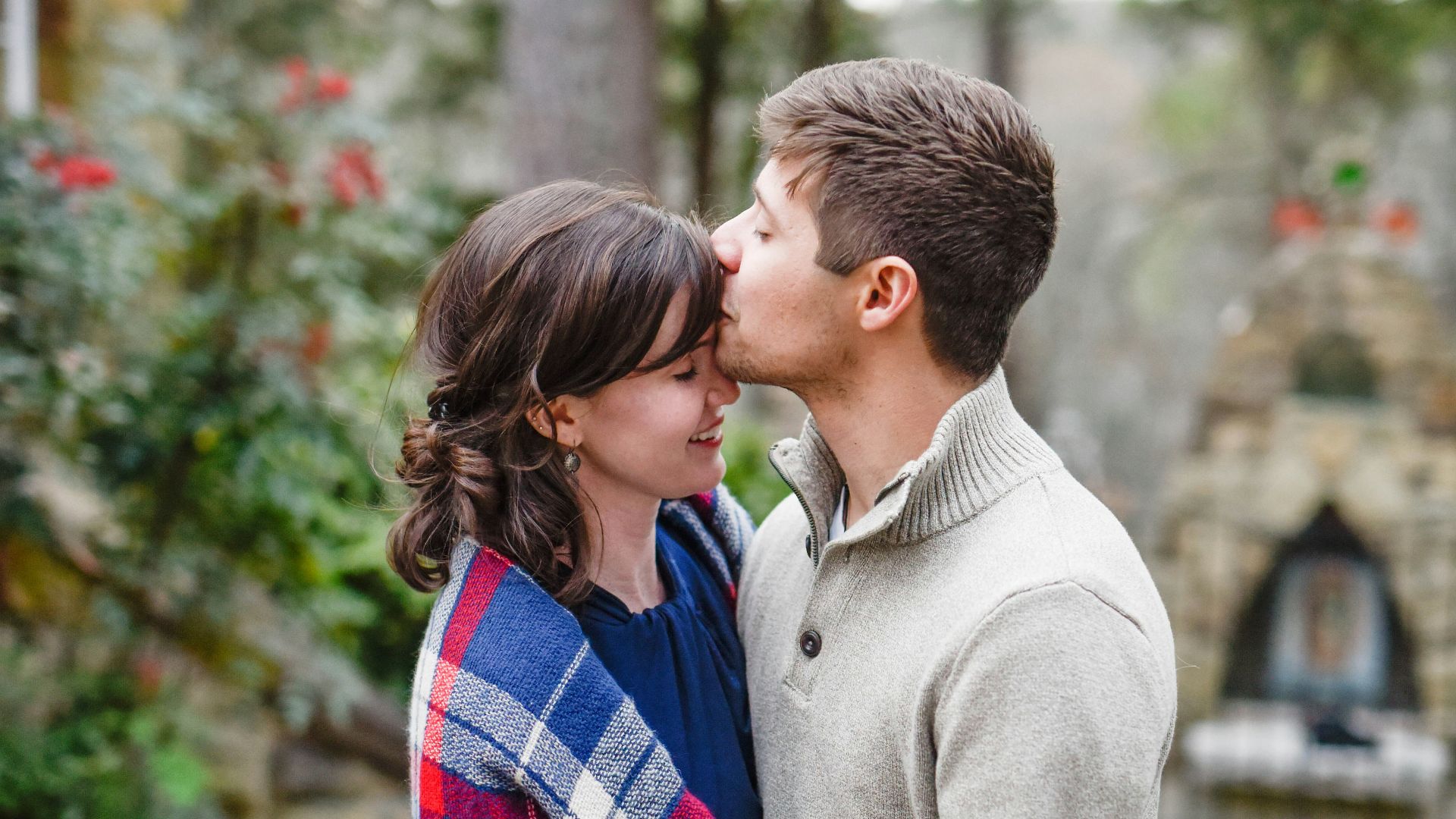 man kissing on woman forehead standing near tree during daytime