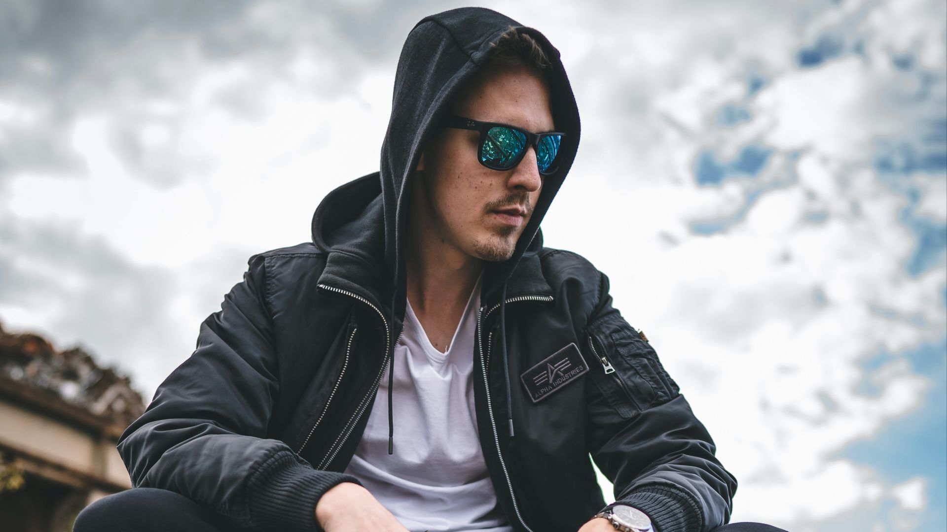 man in black leather jacket and black pants sitting on brown metal wheel during daytime