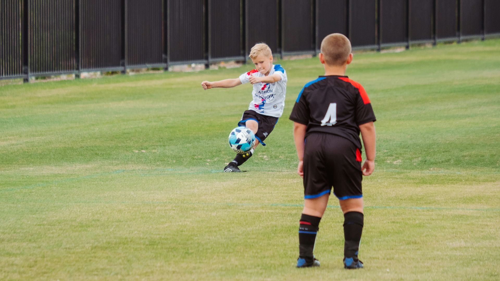 2 boys playing soccer on green grass field during daytime
