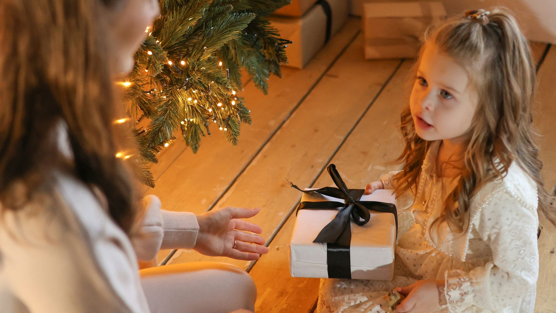 A little girl sitting on the floor next to a christmas tree