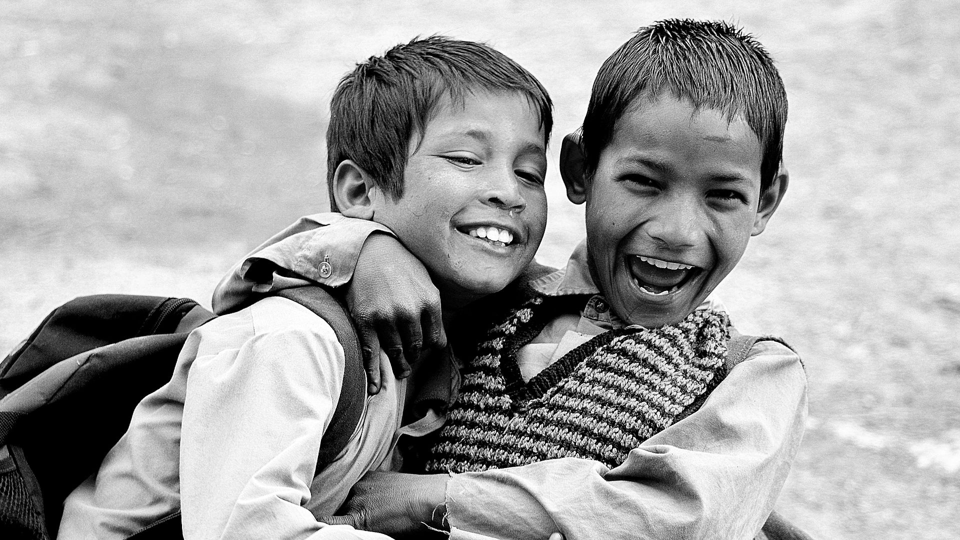 grayscale photography of two boys hugging while laughing