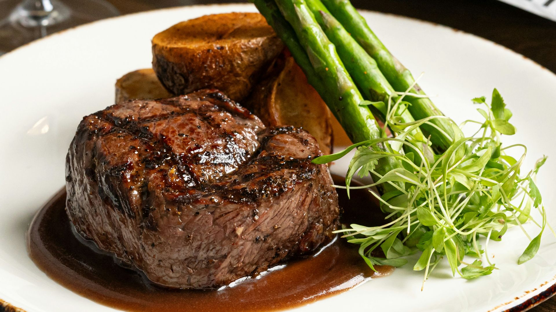 a plate of steak and asparagus with a glass of wine