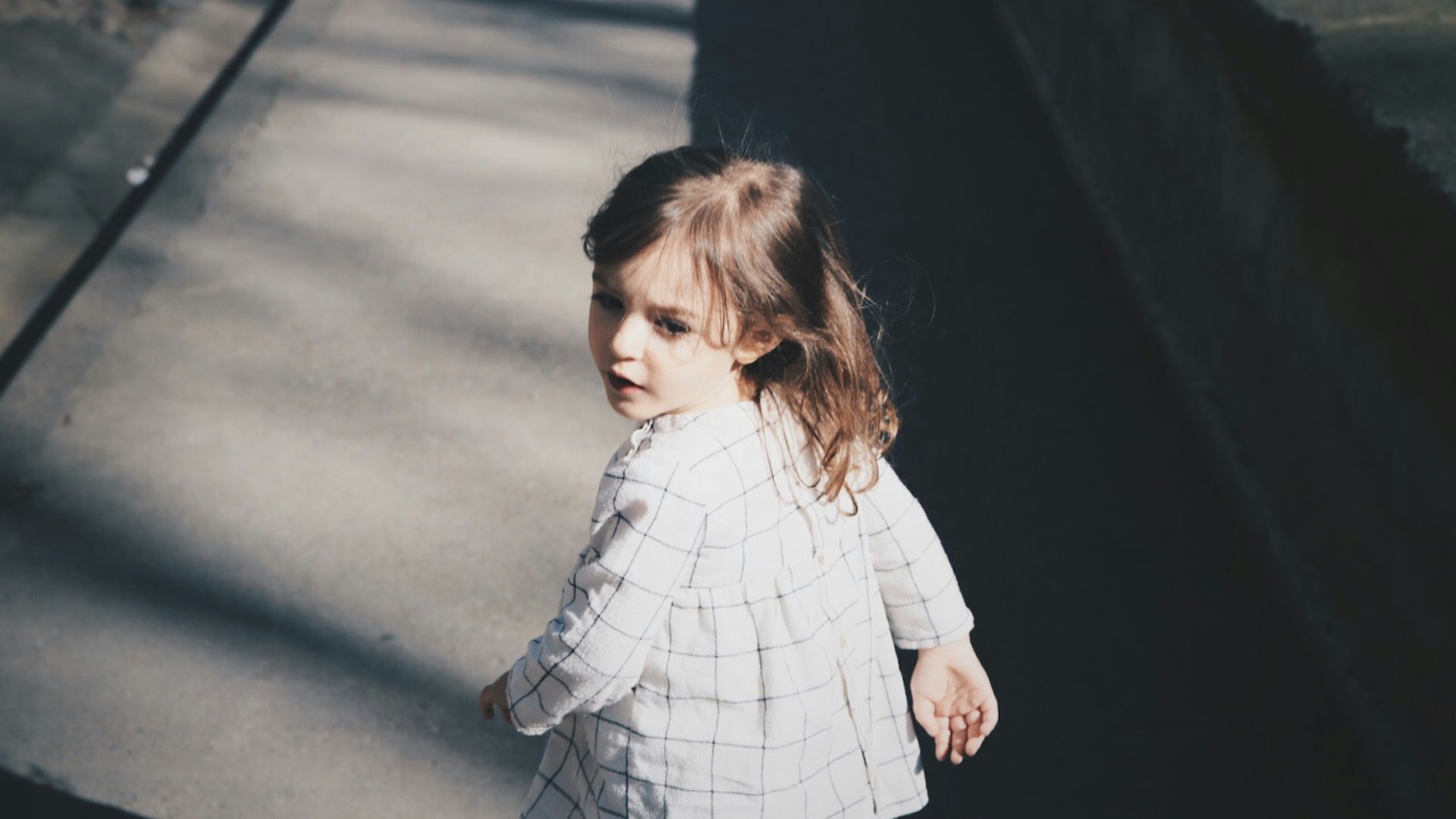 toddler girl walking on gray concrete road at daytime