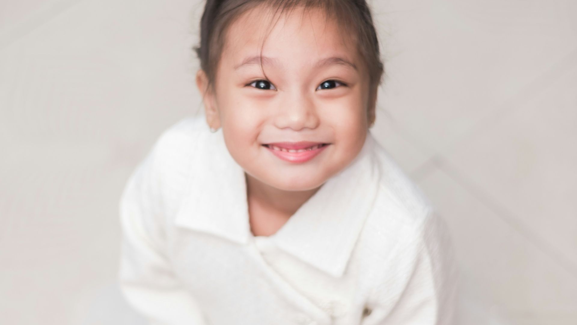 a little girl sitting on the floor in a white dress
