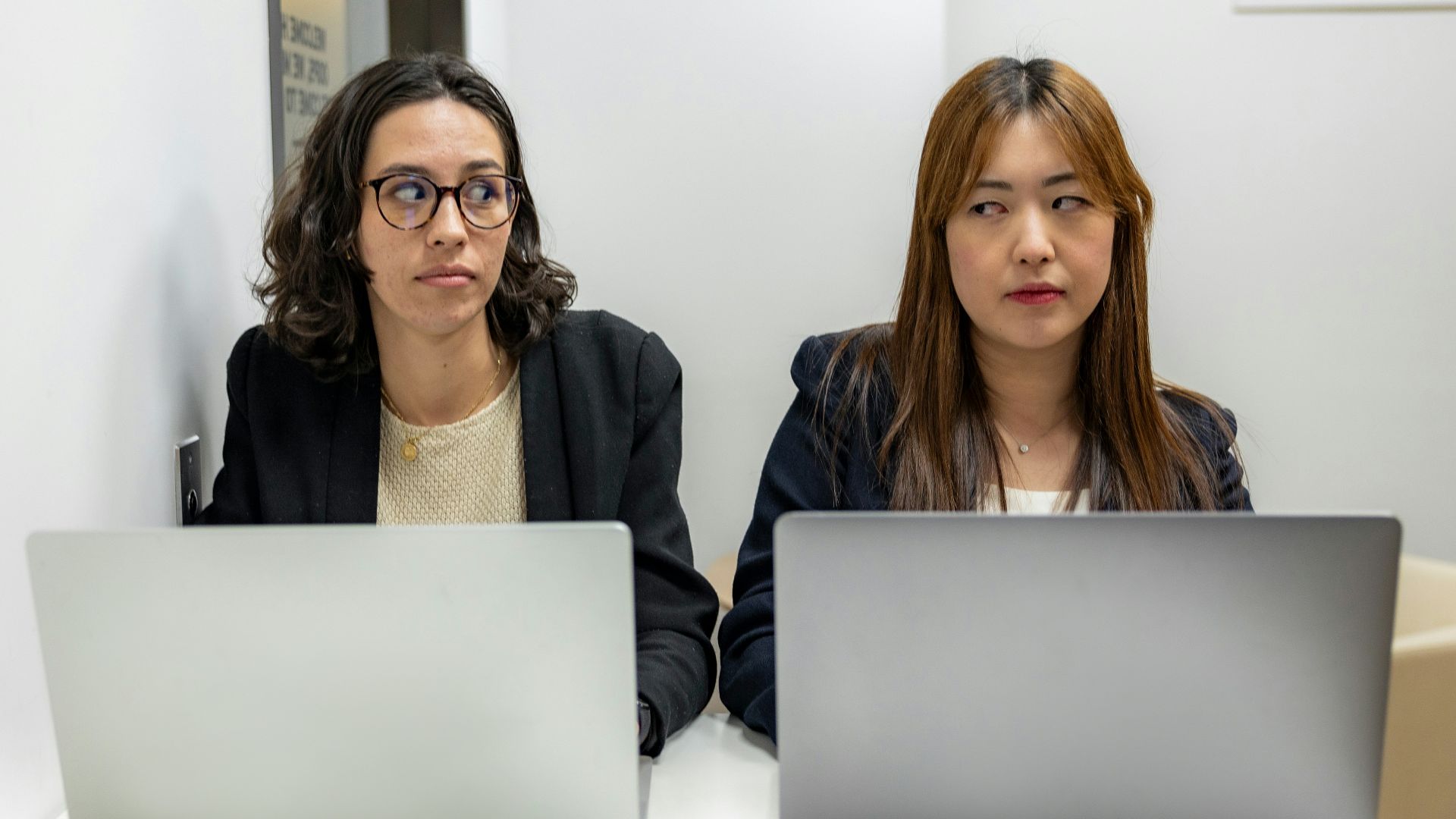 two women sitting at a table with laptops