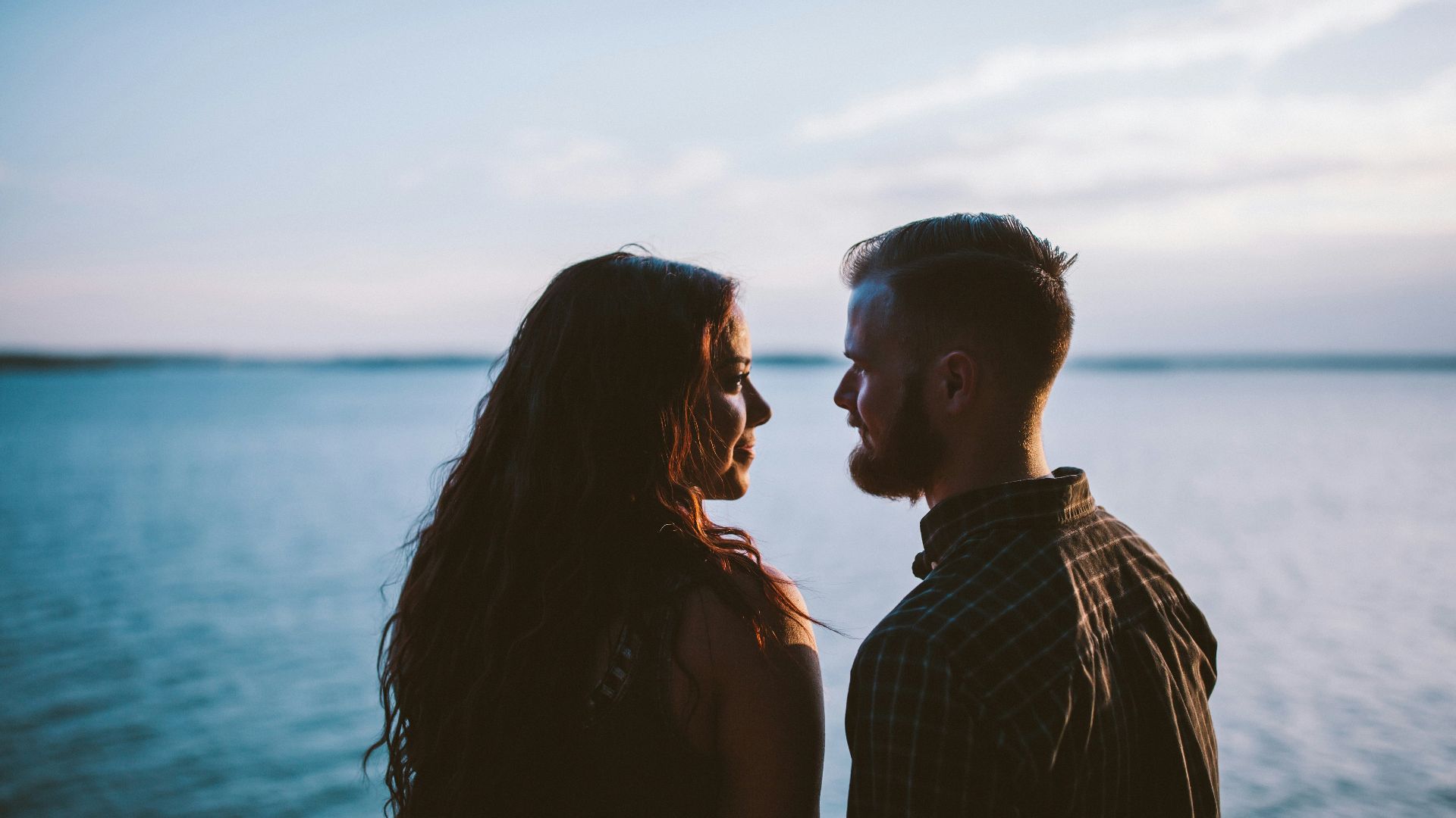 man and woman standing while looking each other near body of water
