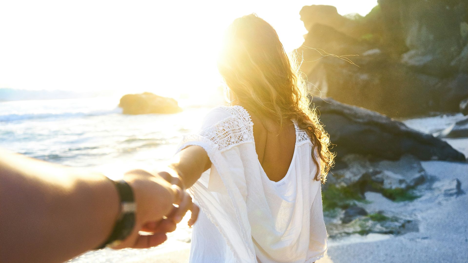 person holding woman's hand beside sea while facing sunlight