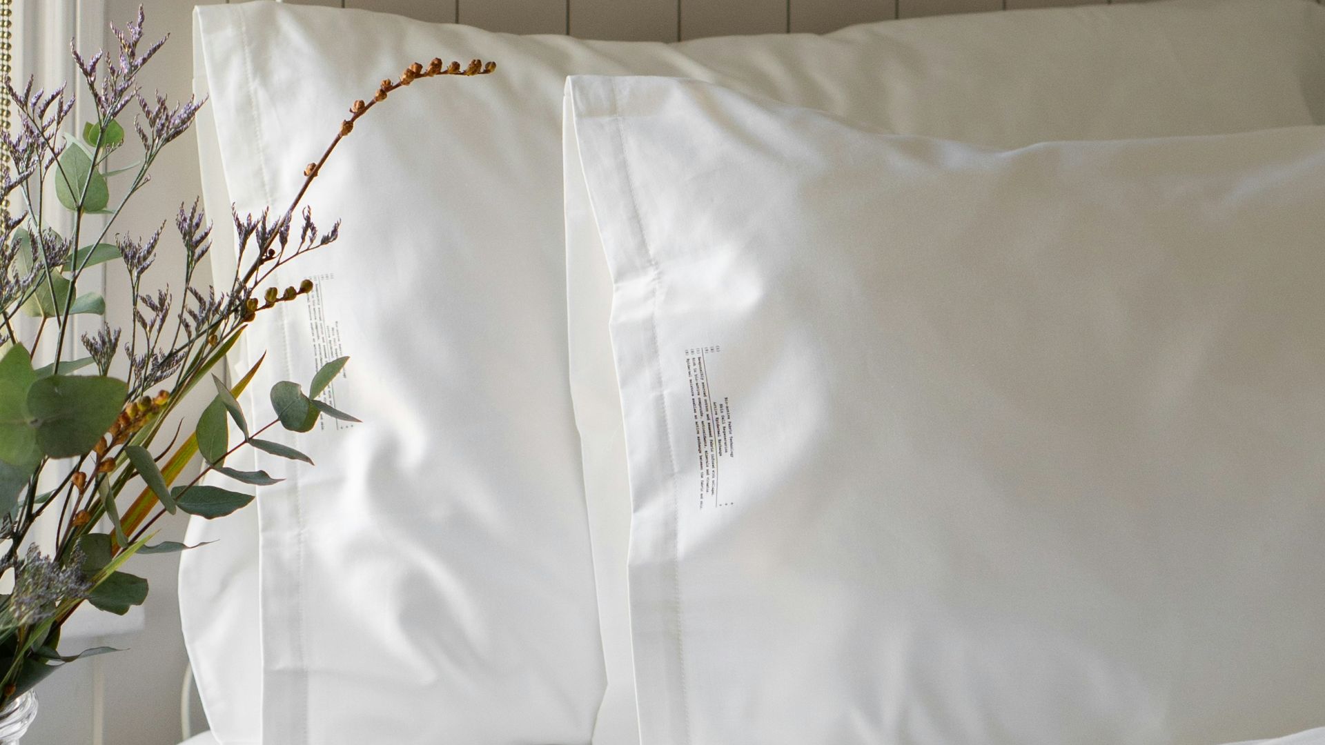 a bed with white sheets and pillows and a vase with flowers
