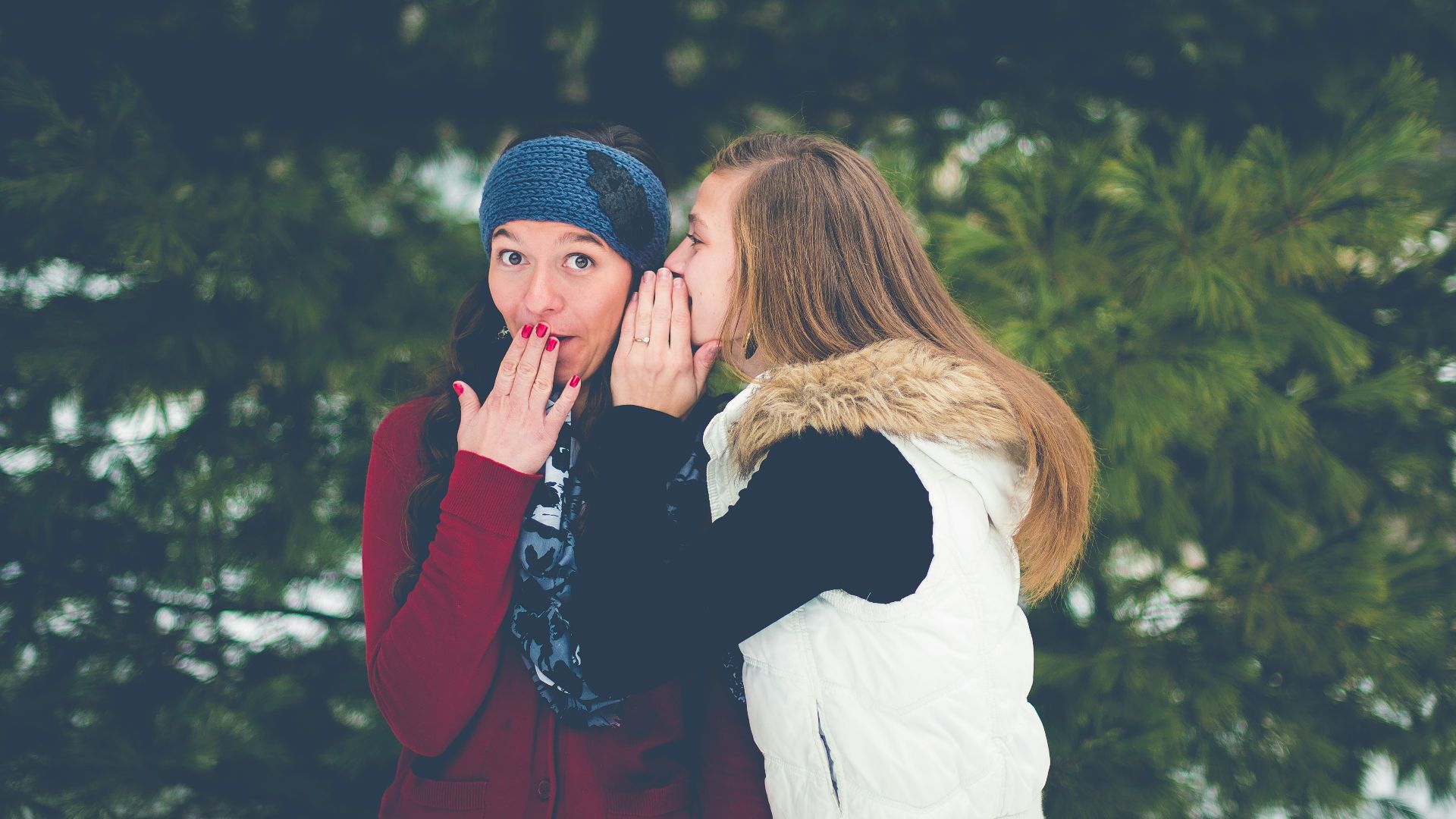woman whispering on woman's ear while hands on lips