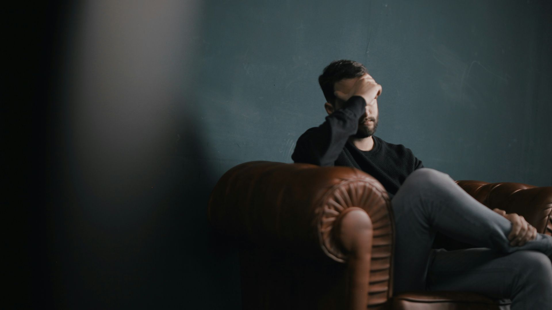 a man holds his head while sitting on a sofa