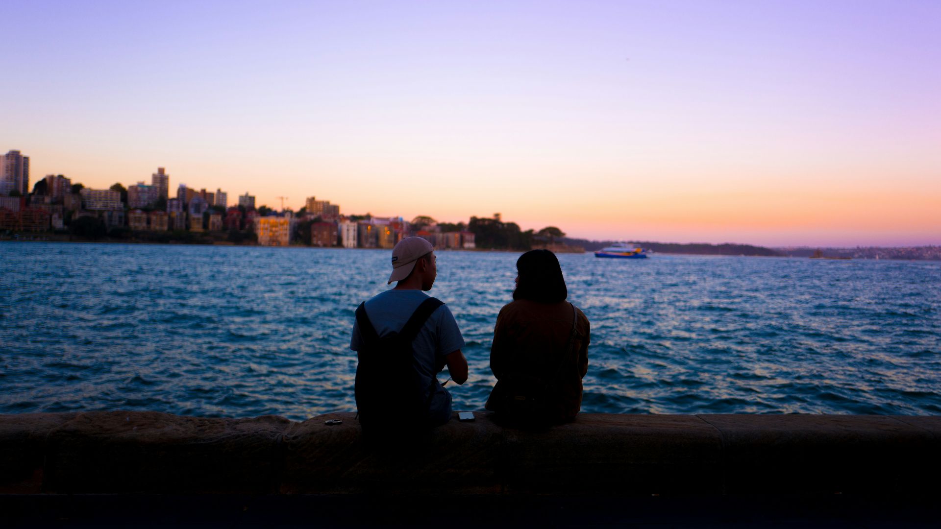 man and woman sitting facing body of water