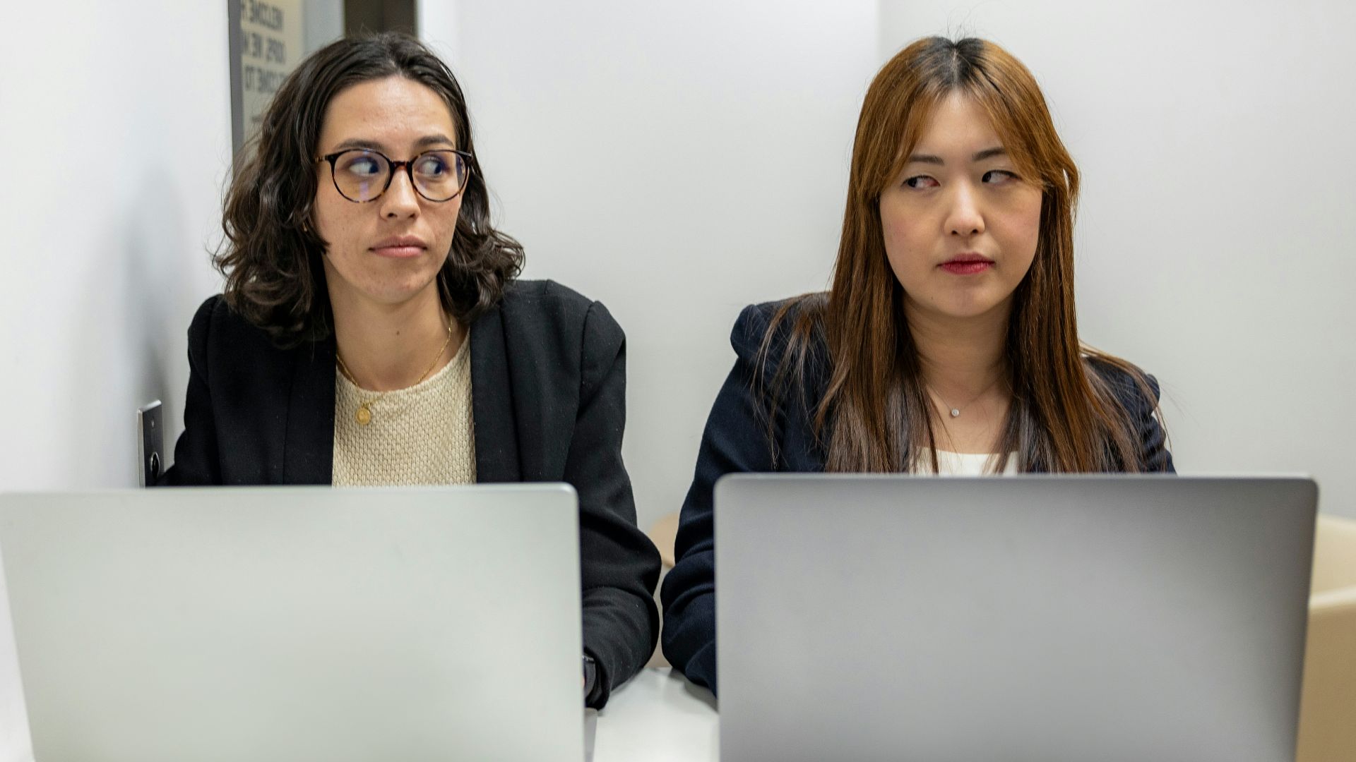 two women sitting at a table with laptops