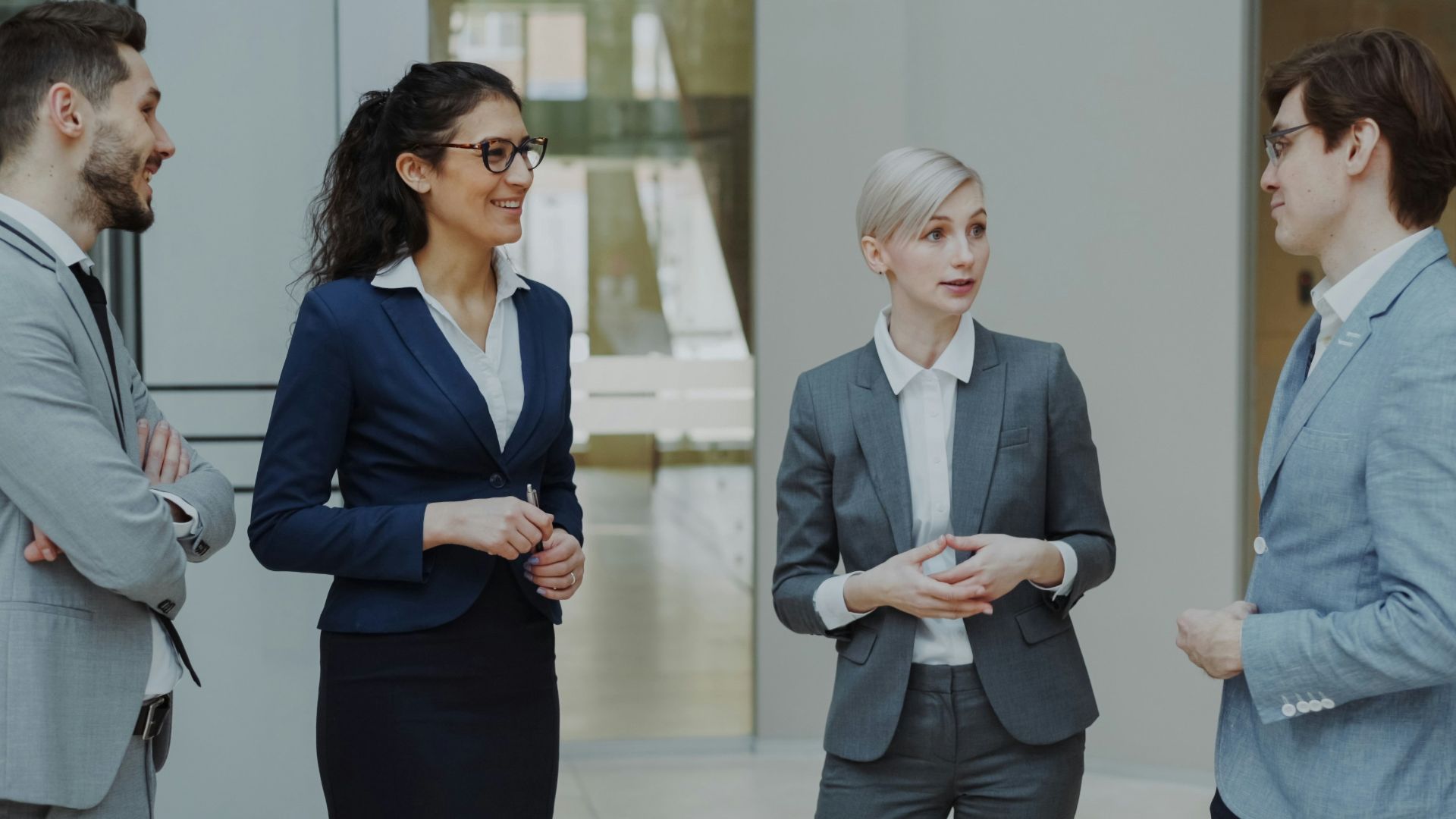 Four business professionals conversing in a modern office lobby.