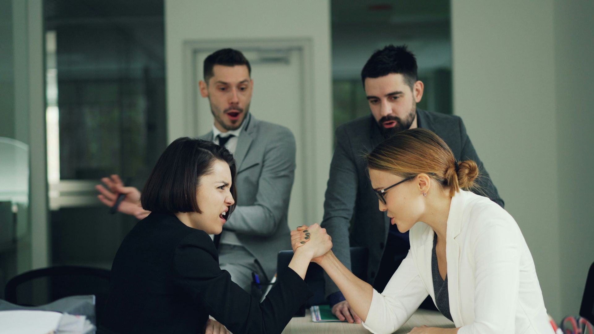 Two women arm wrestling with men watching