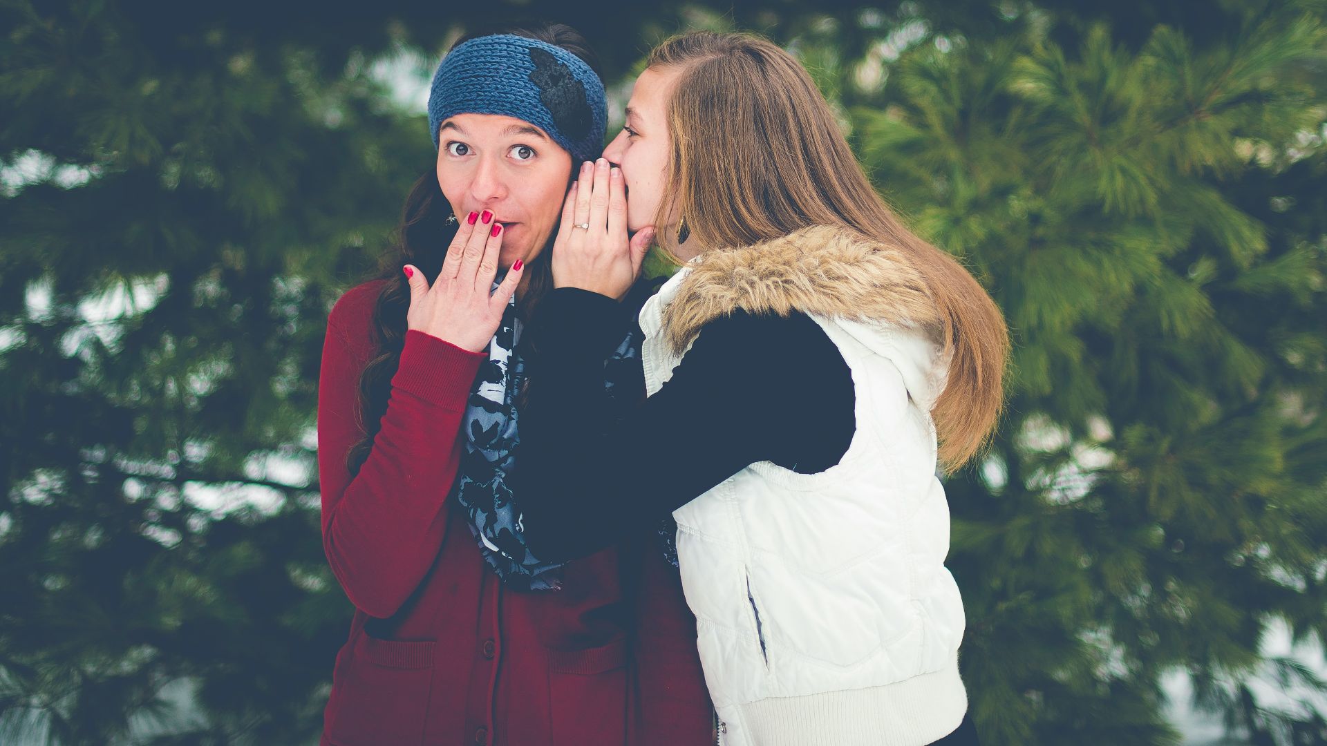 woman whispering on woman's ear while hands on lips