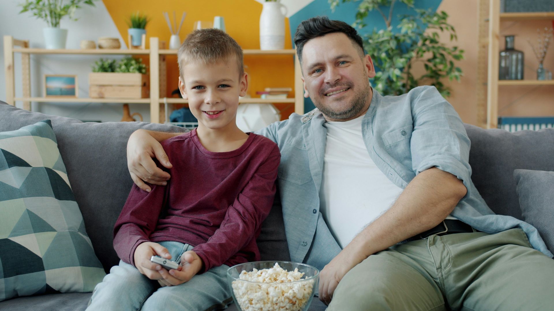 Father and son smiling on the couch with popcorn.