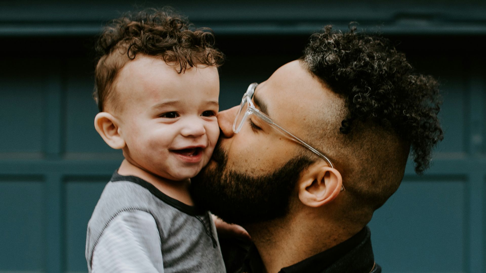 man carrying baby boy and kissing on cheek