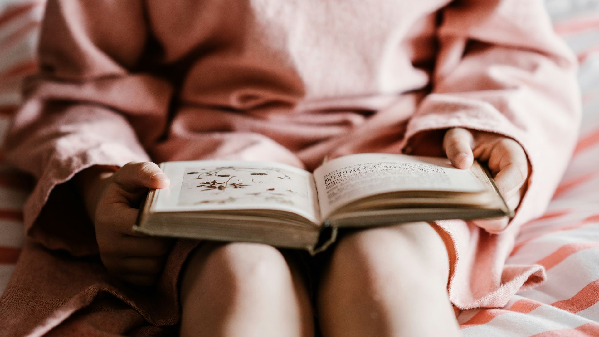 person reading book sitting on red and white striped bedspread