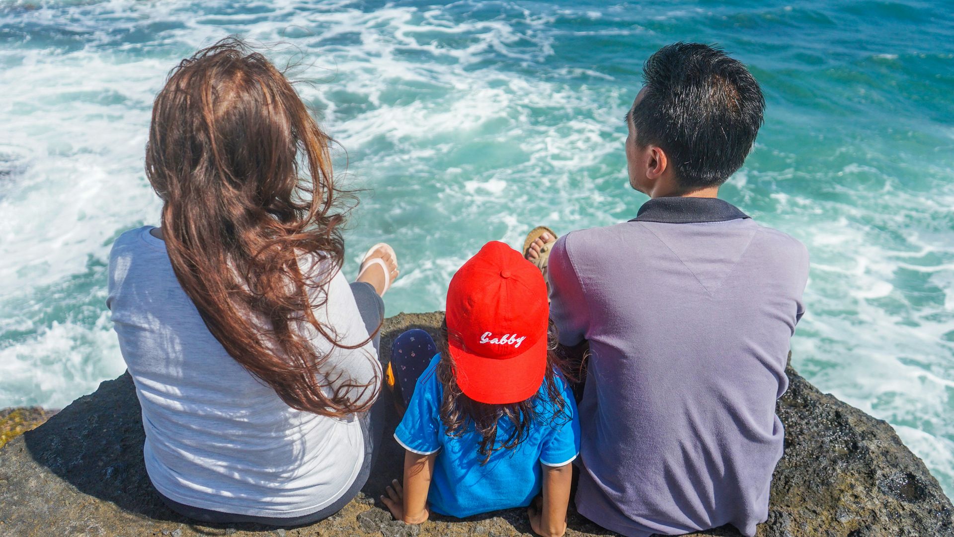 man and woman sitting on rock near body of water during daytime
