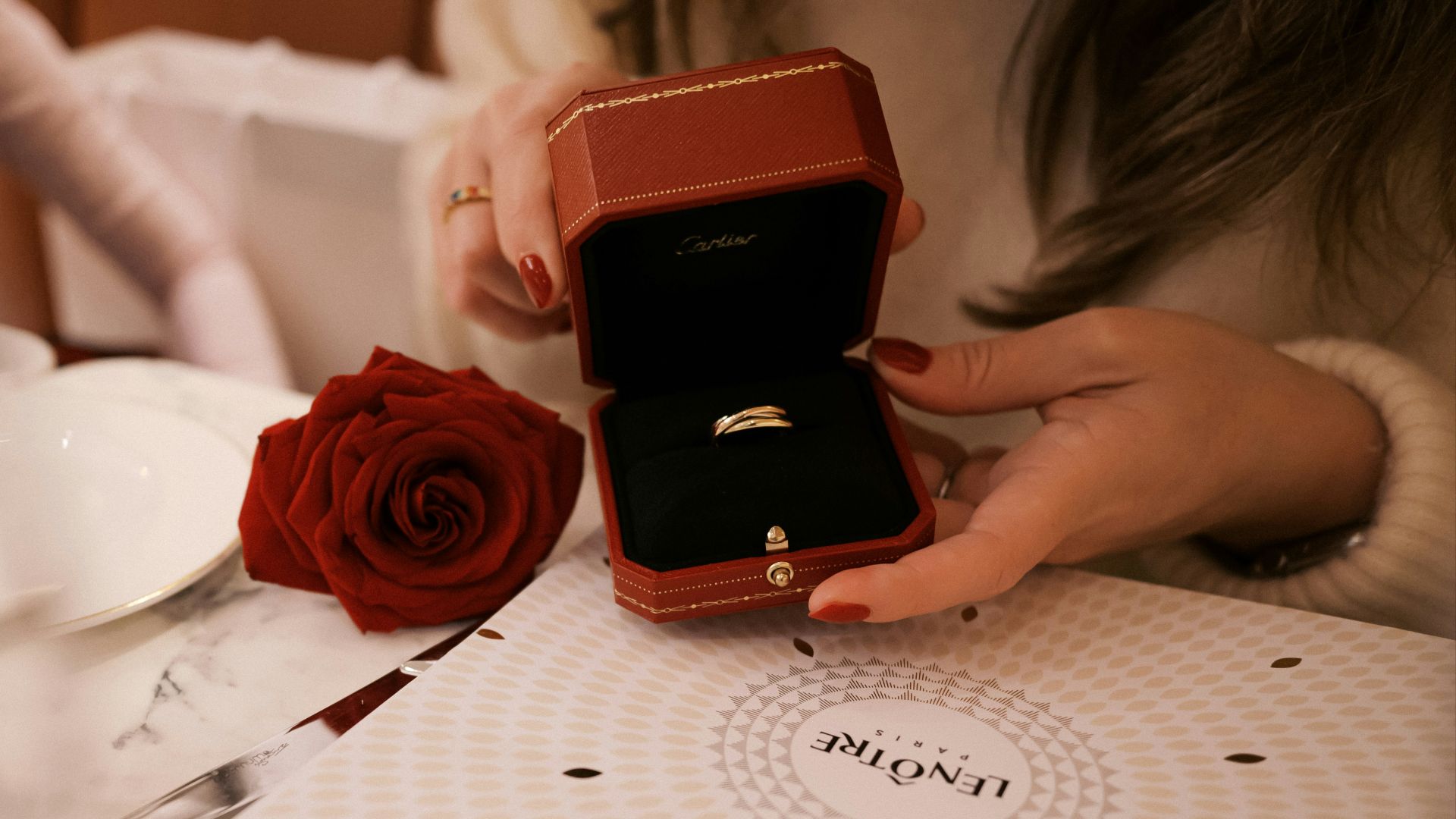 A woman sitting at a table holding a ring box