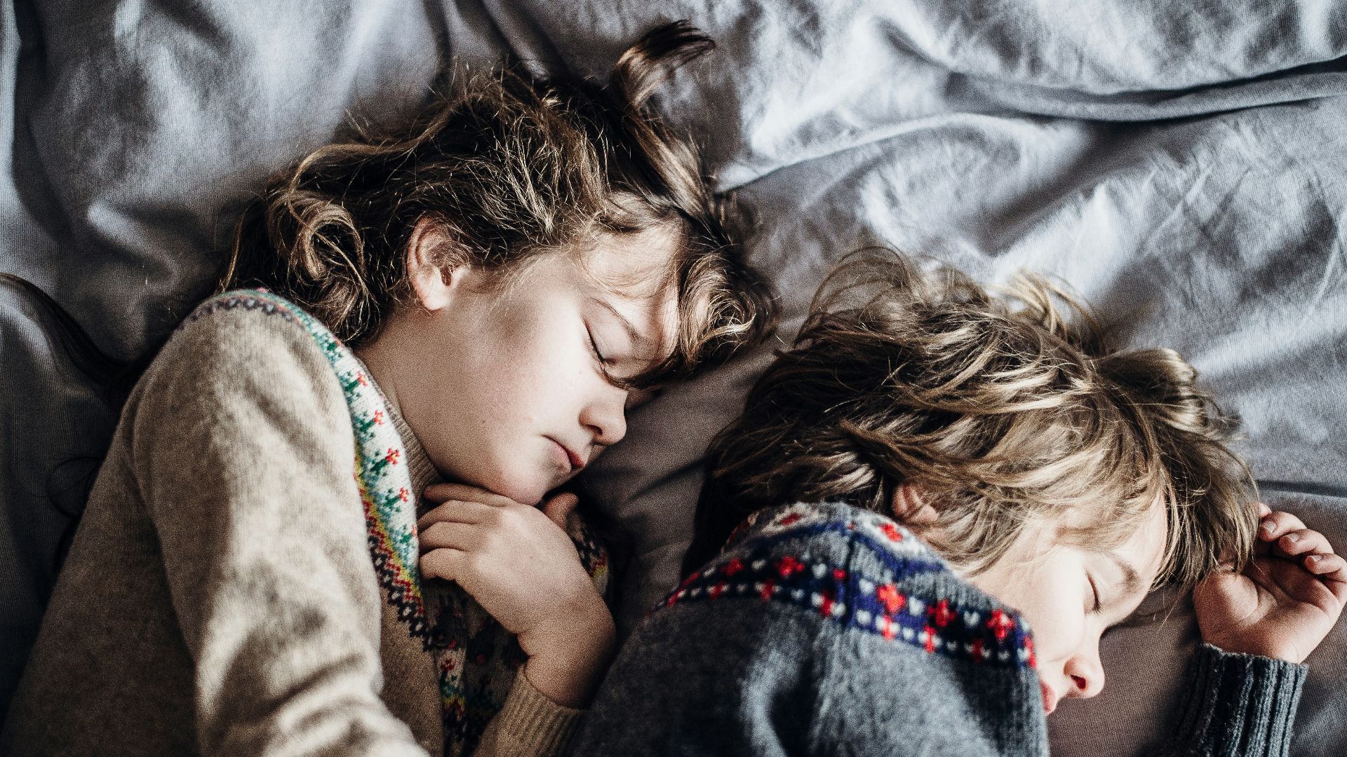 two girls wearing brown and gray knitted sweaters lying on gray textile