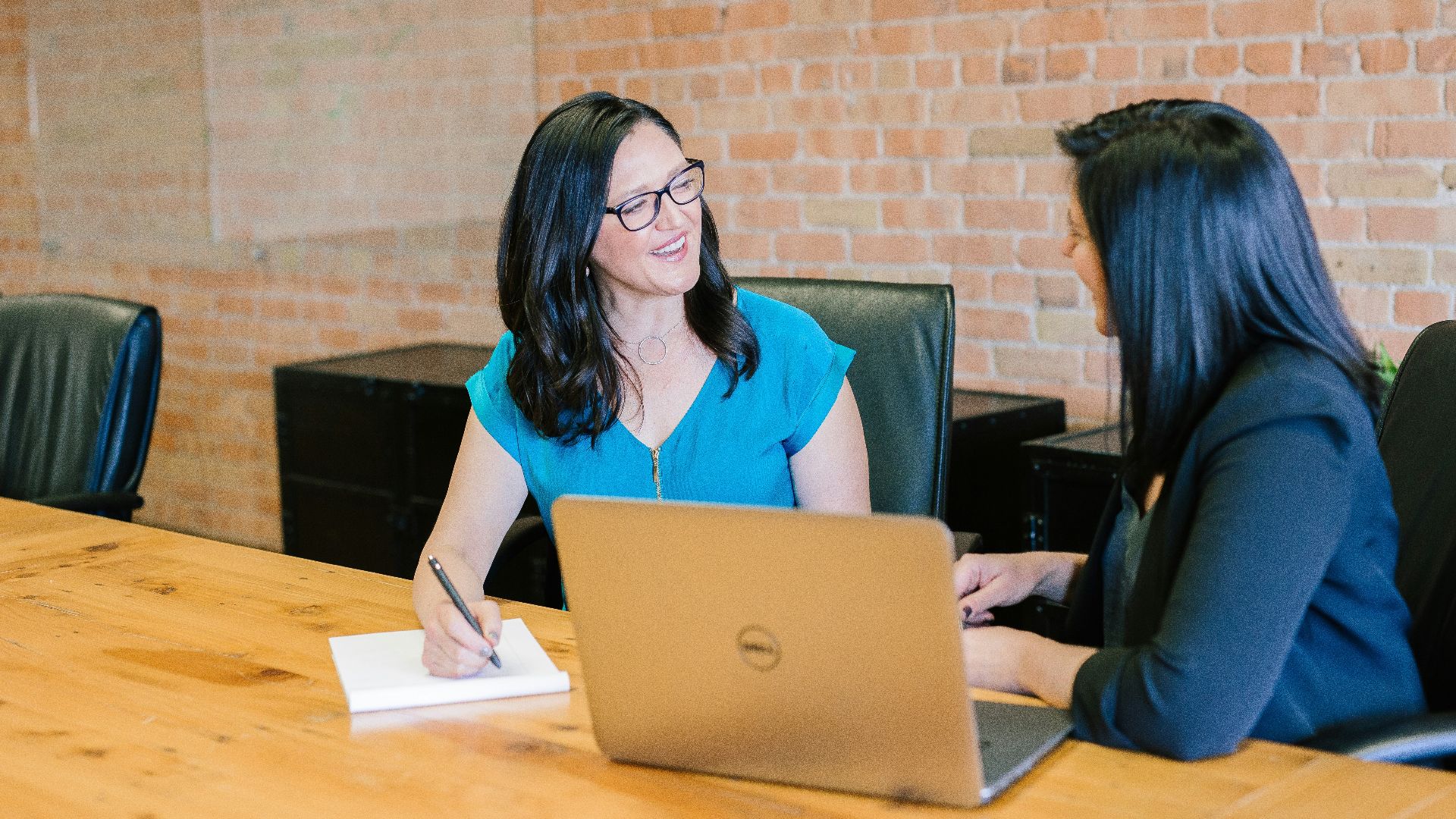 woman in teal t-shirt sitting beside woman in suit jacket