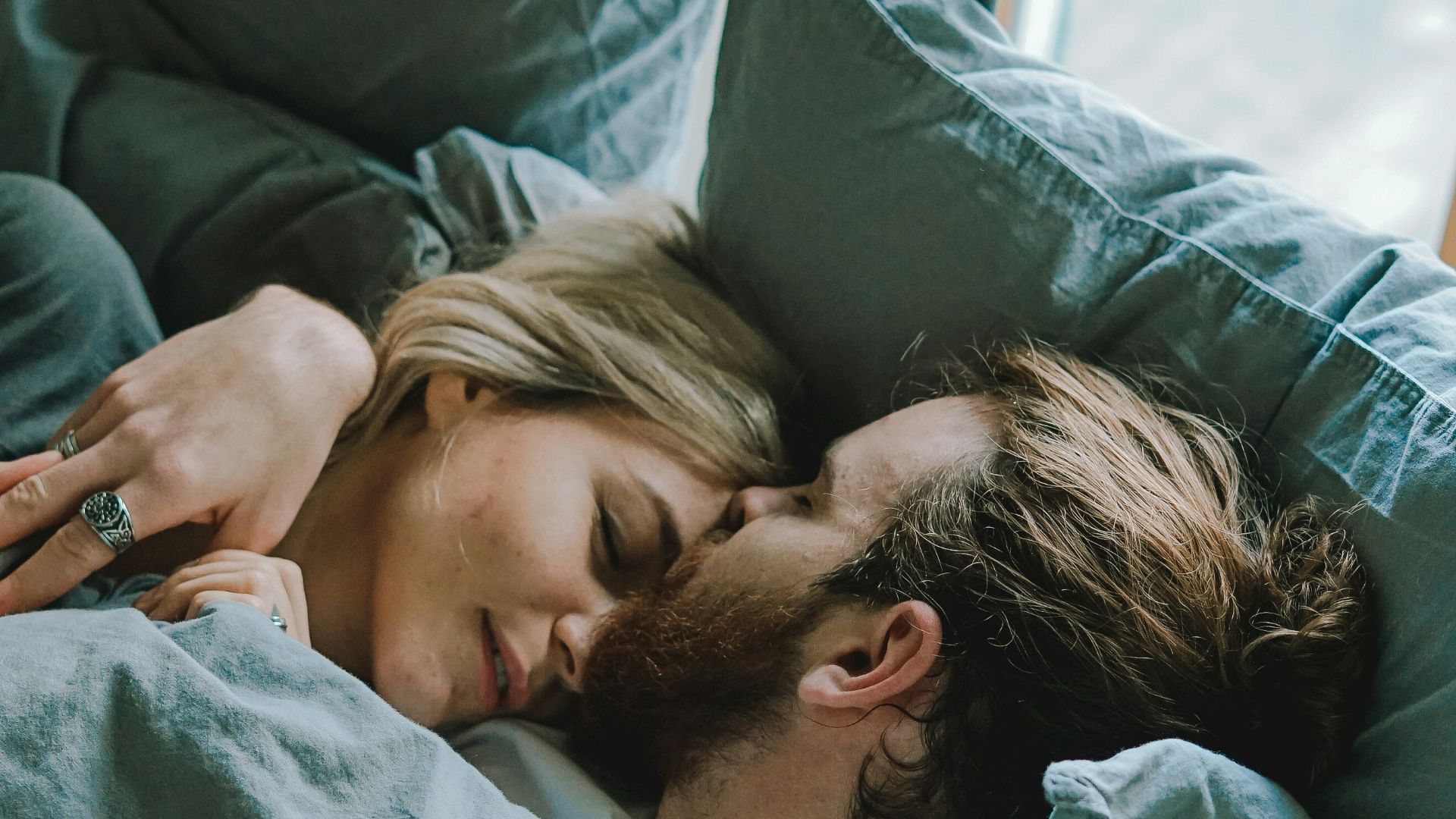 man kissing woman's forehead while lying on bed