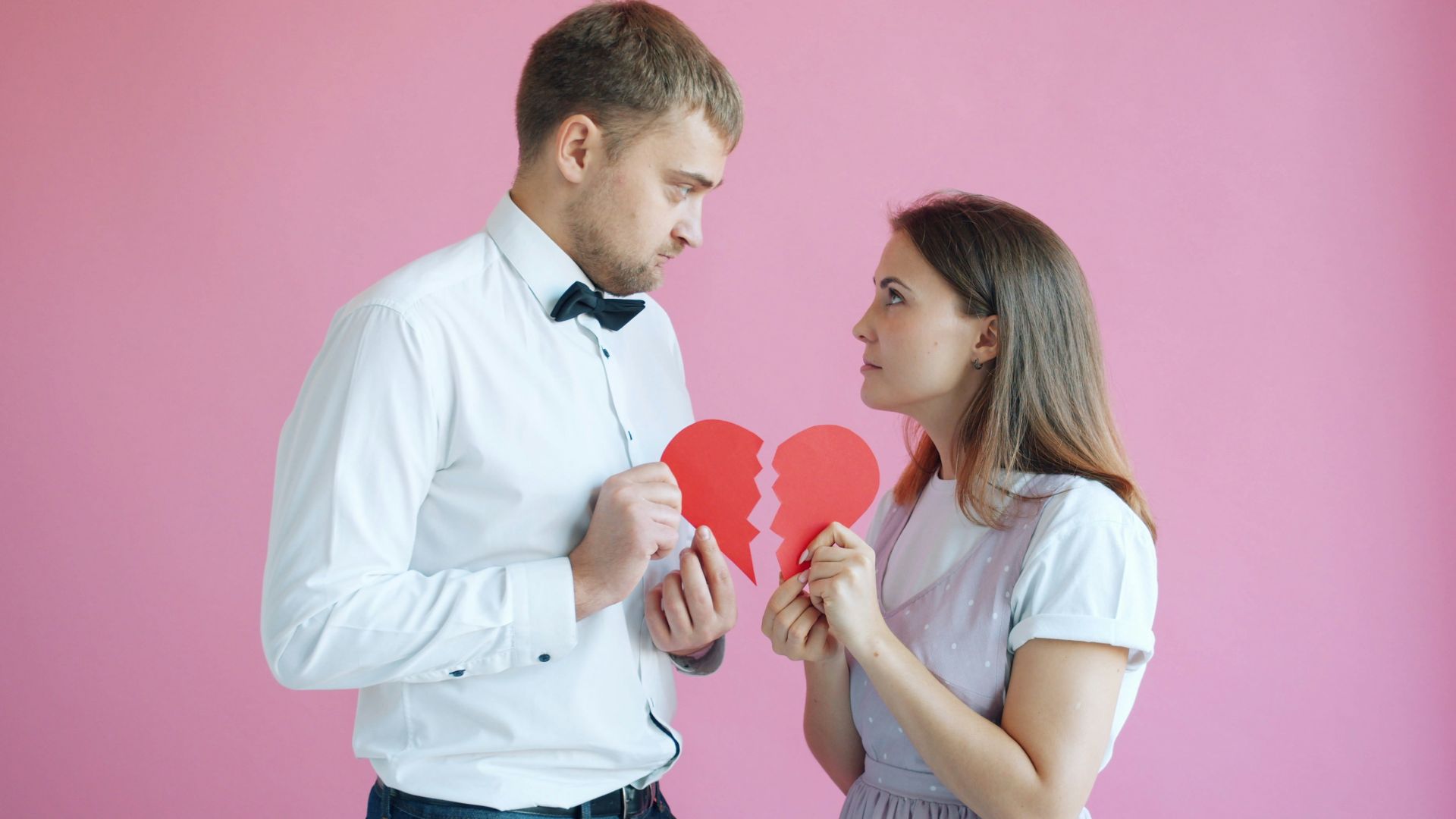 Couple holding broken heart halves on pink background