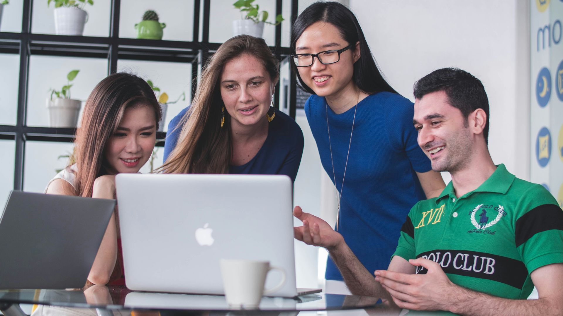 four people watching on white MacBook on top of glass-top table