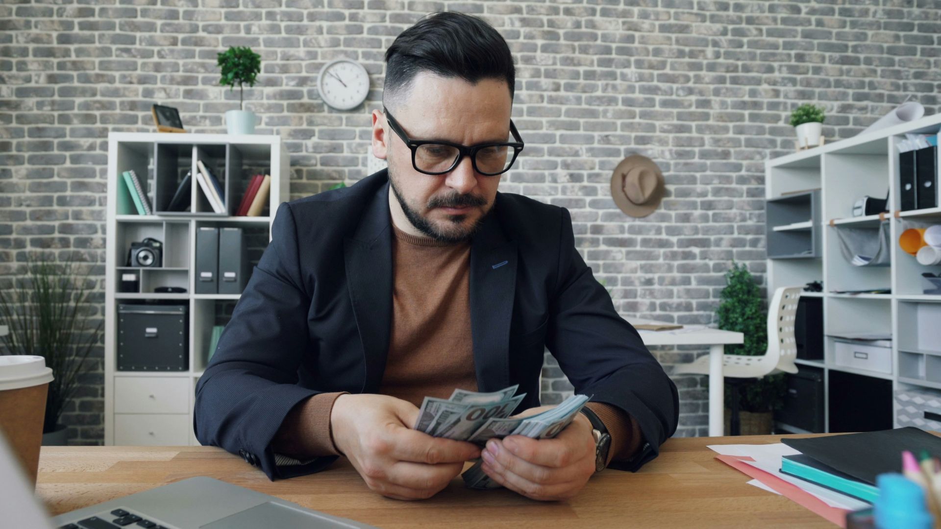 a man sitting at a table with a laptop and money
