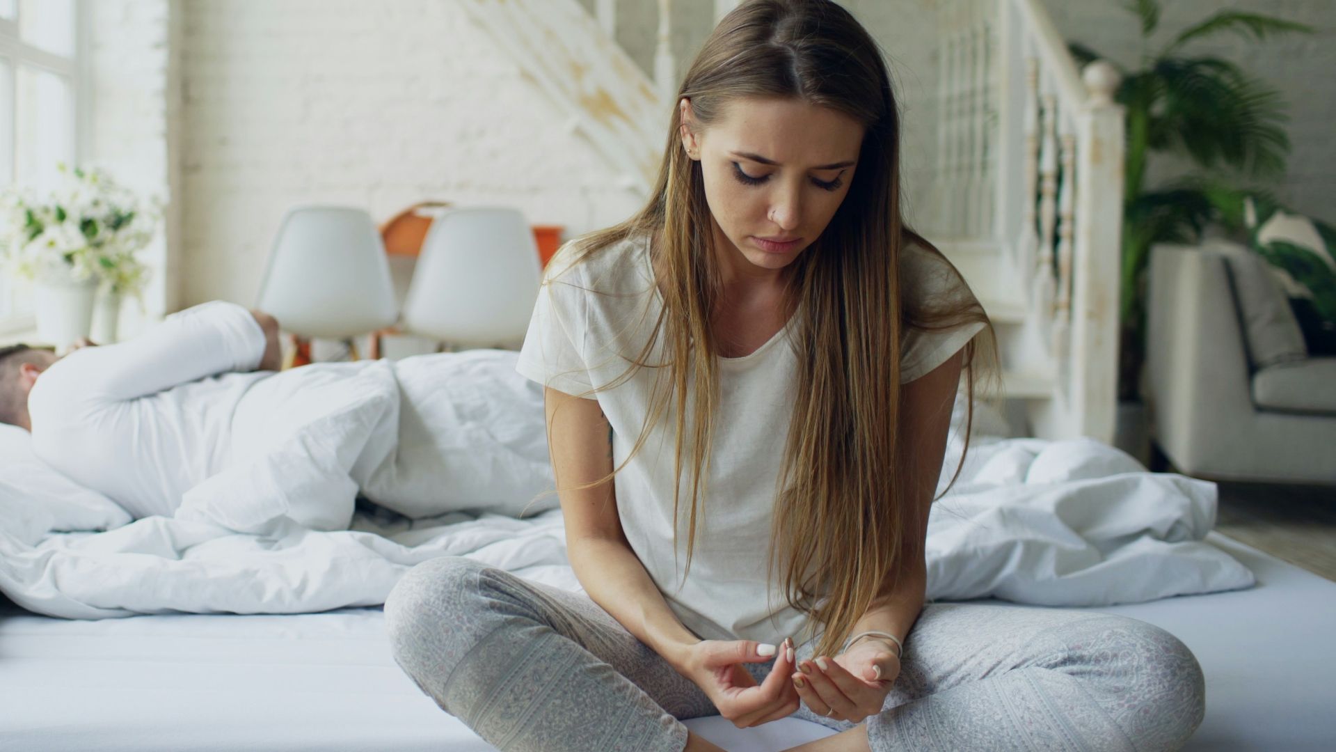 Woman sitting on bed, man sleeping behind her