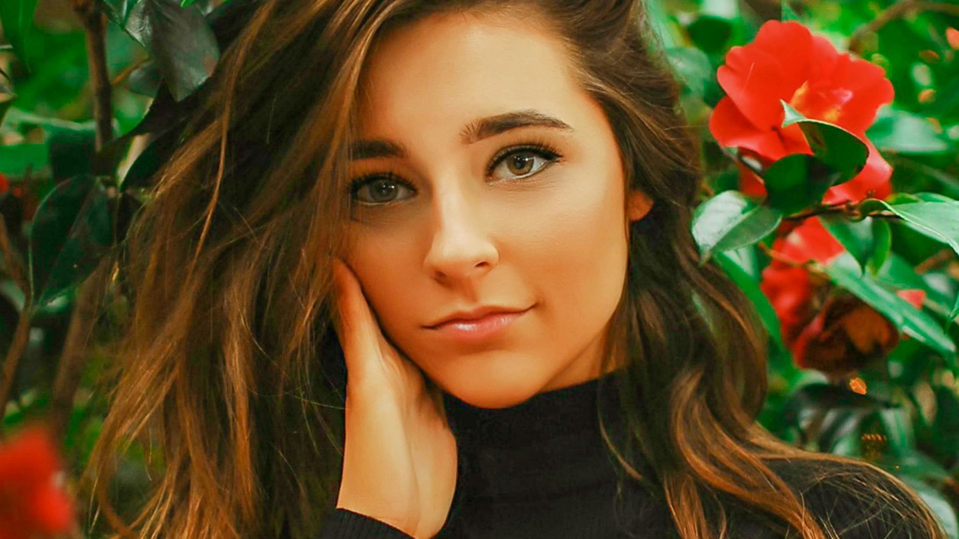 woman standing near red-petaled flowers while left hand oncheek