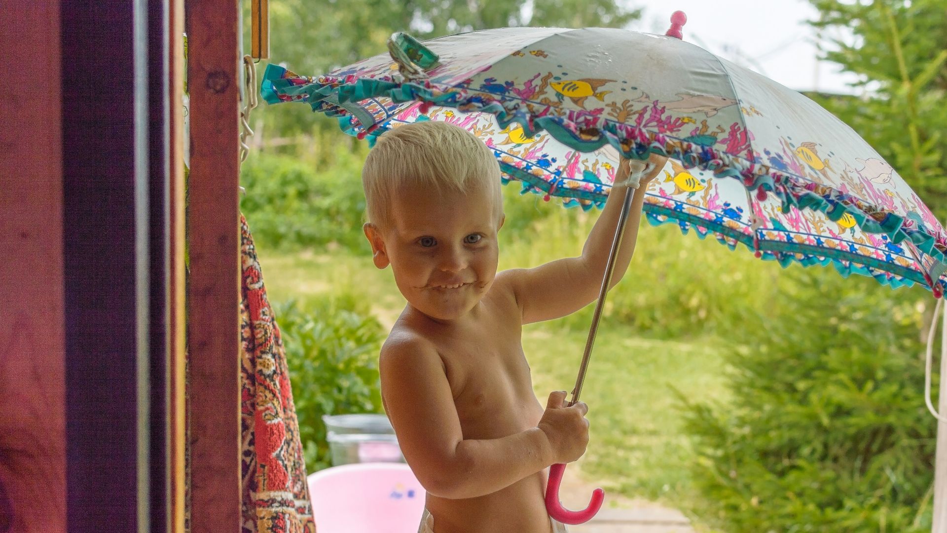 topless baby holding umbrella while sitting on concrete floor during daytime